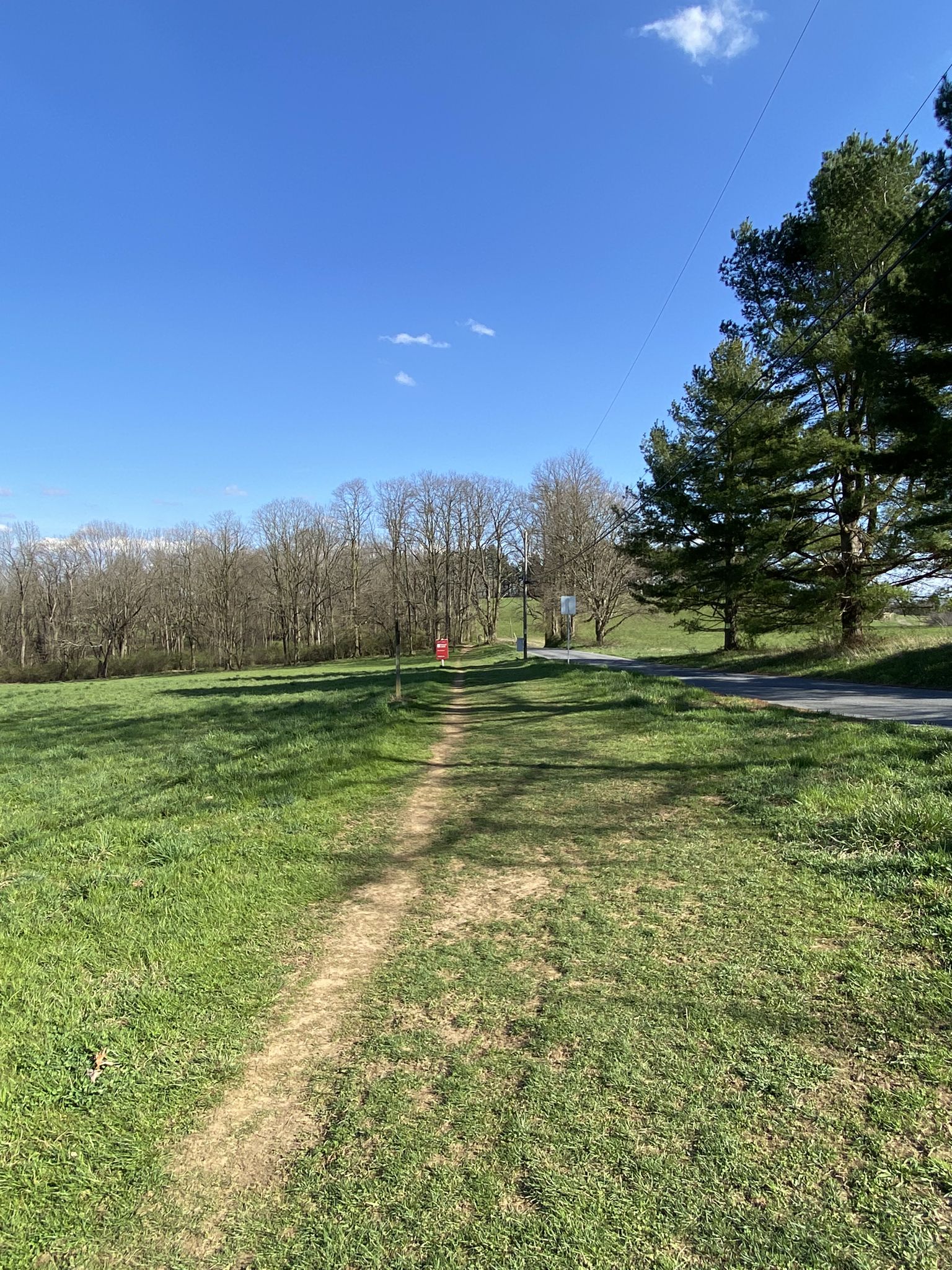 Narrow dirt path through a sunny grassy field with distant trees and road. - Chester Valley Trail – Battle of the Clouds Park loop from Malvern