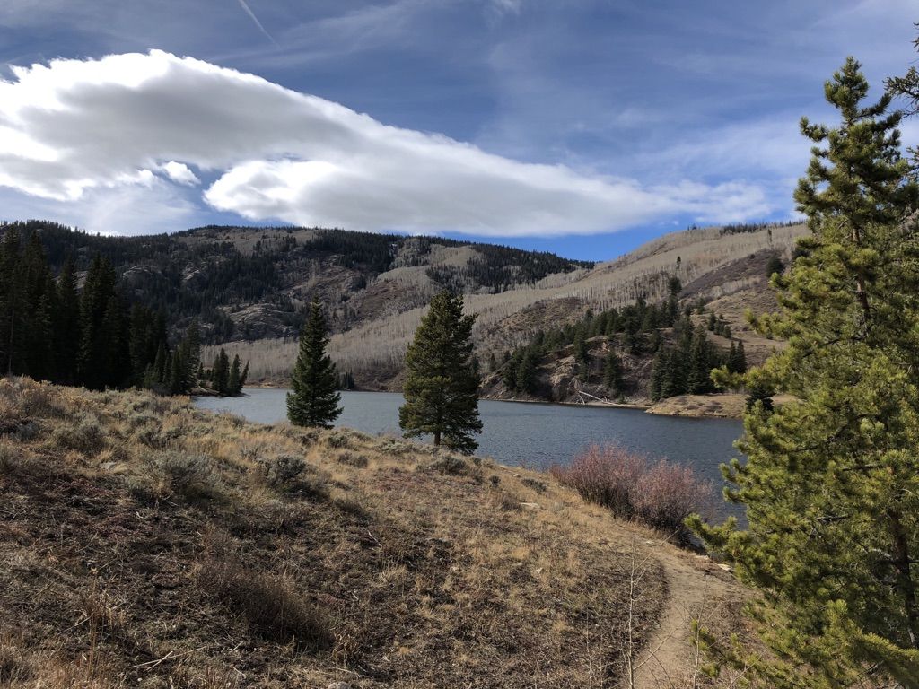 A serene lake surrounded by forested mountains under a partly cloudy sky. - Lower Cataract Lake Loop