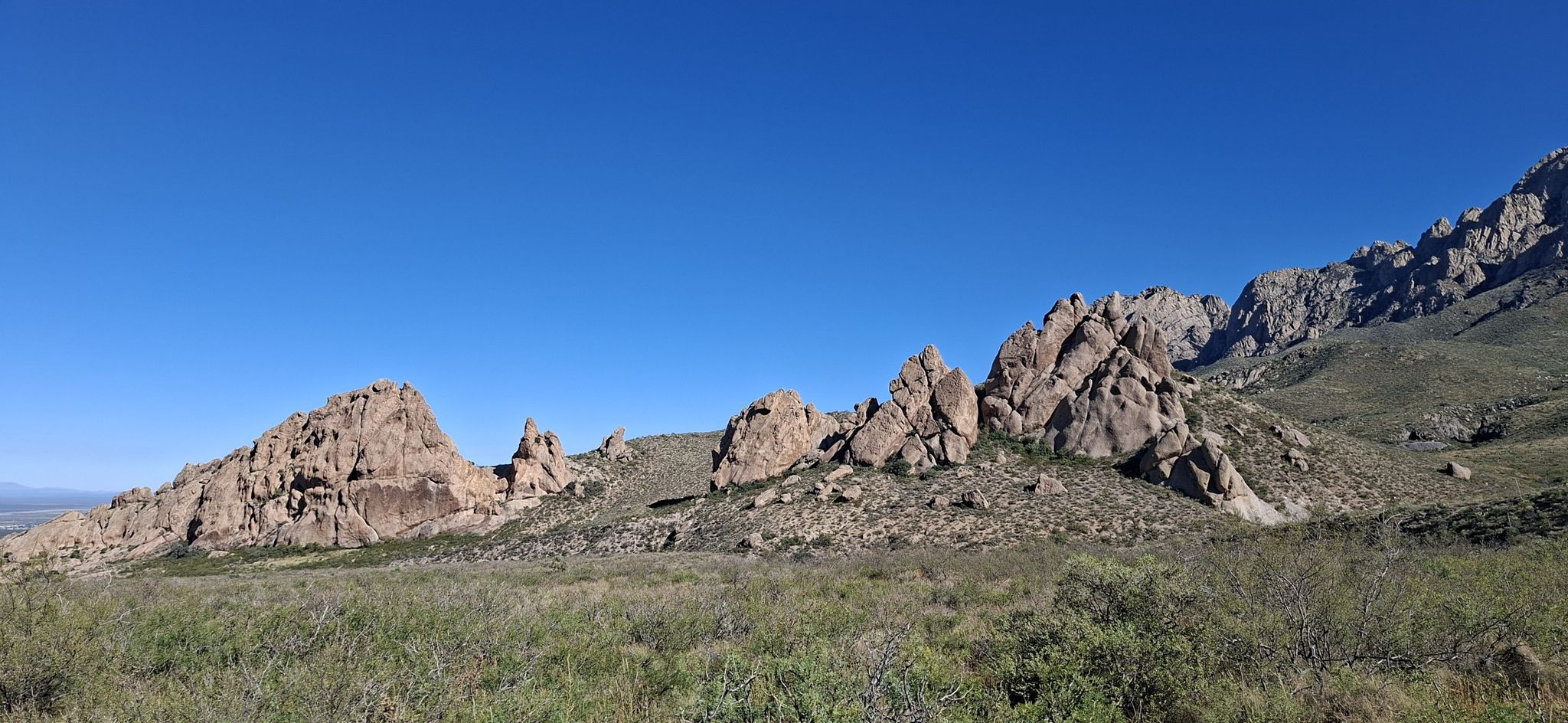 Rocky mountainside with sparse green vegetation under a clear blue sky. - La Cueva Loop Trail