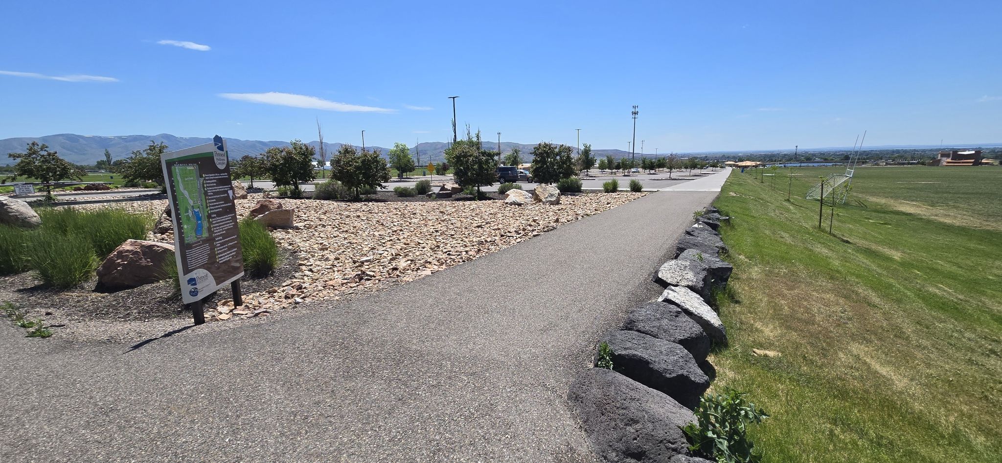 Paved path next to rocks and grass, distant mountains under a clear sky. - Portneuf Wellness Complex Loop