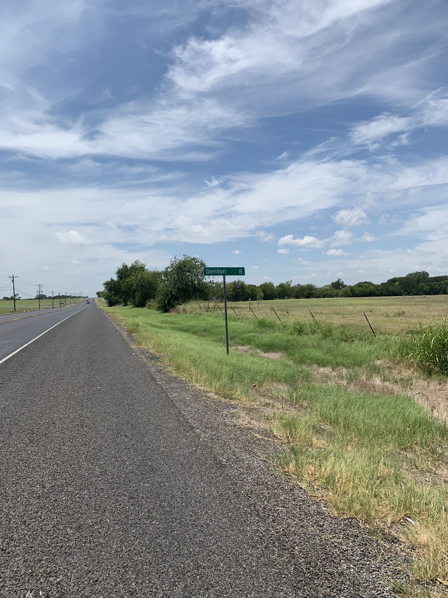 A paved road next to a grassy field under a cloudy blue sky. - Denton to Little Elm loop via Lewisville Lake toll bridge