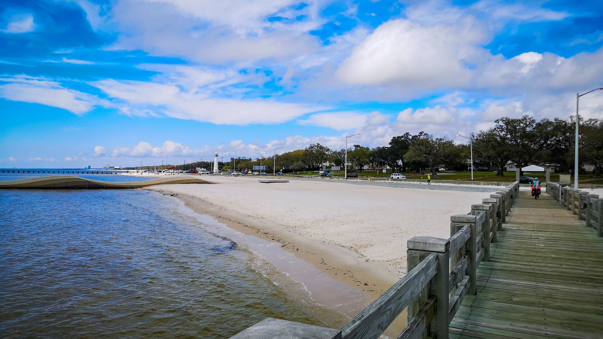 Sunny beach with calm water, a long pier, and distant buildings under blue sky. - Biloxi Bay Bridge and Boardwalk Loop