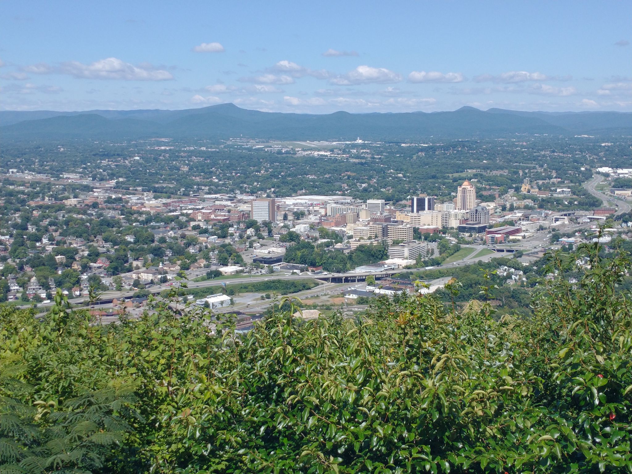 Panoramic view of a city with distant mountains under a clear sky. - Mill Mountain Park Loop