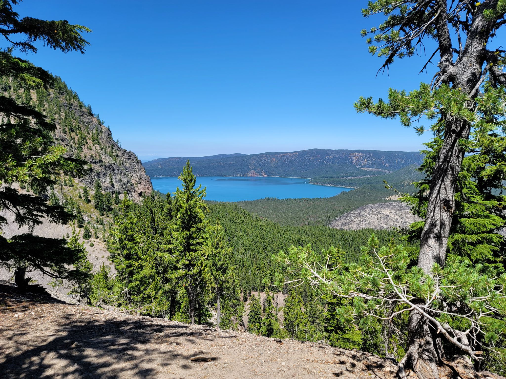 Bright blue lake nestled among green forests and steep mountains on a clear day. - Crater Rim Trail