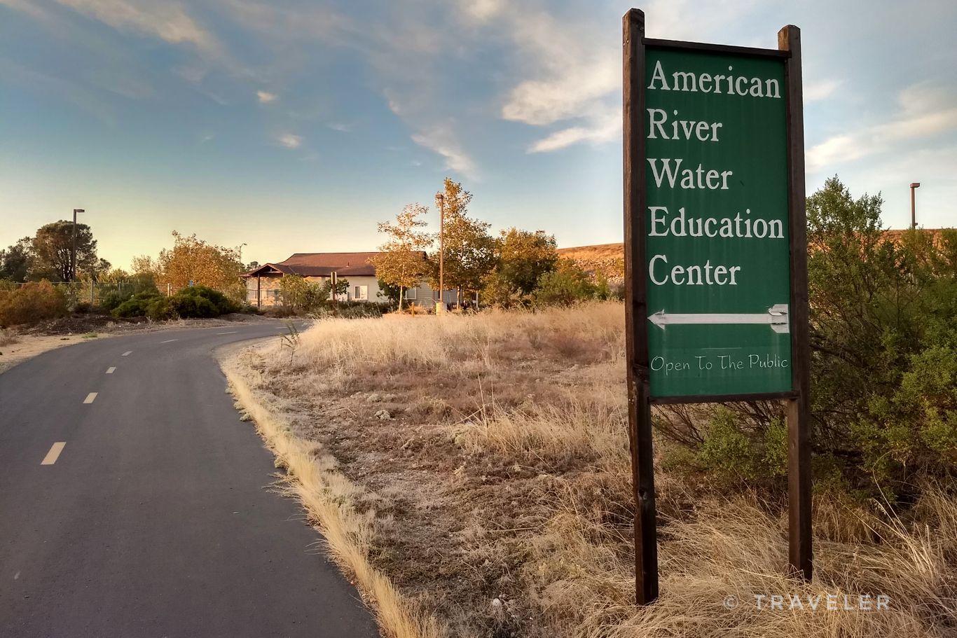 Green sign pointing right next to a paved road, dry grass, warm light. - American River Bike Trail via South Cirby Way loop