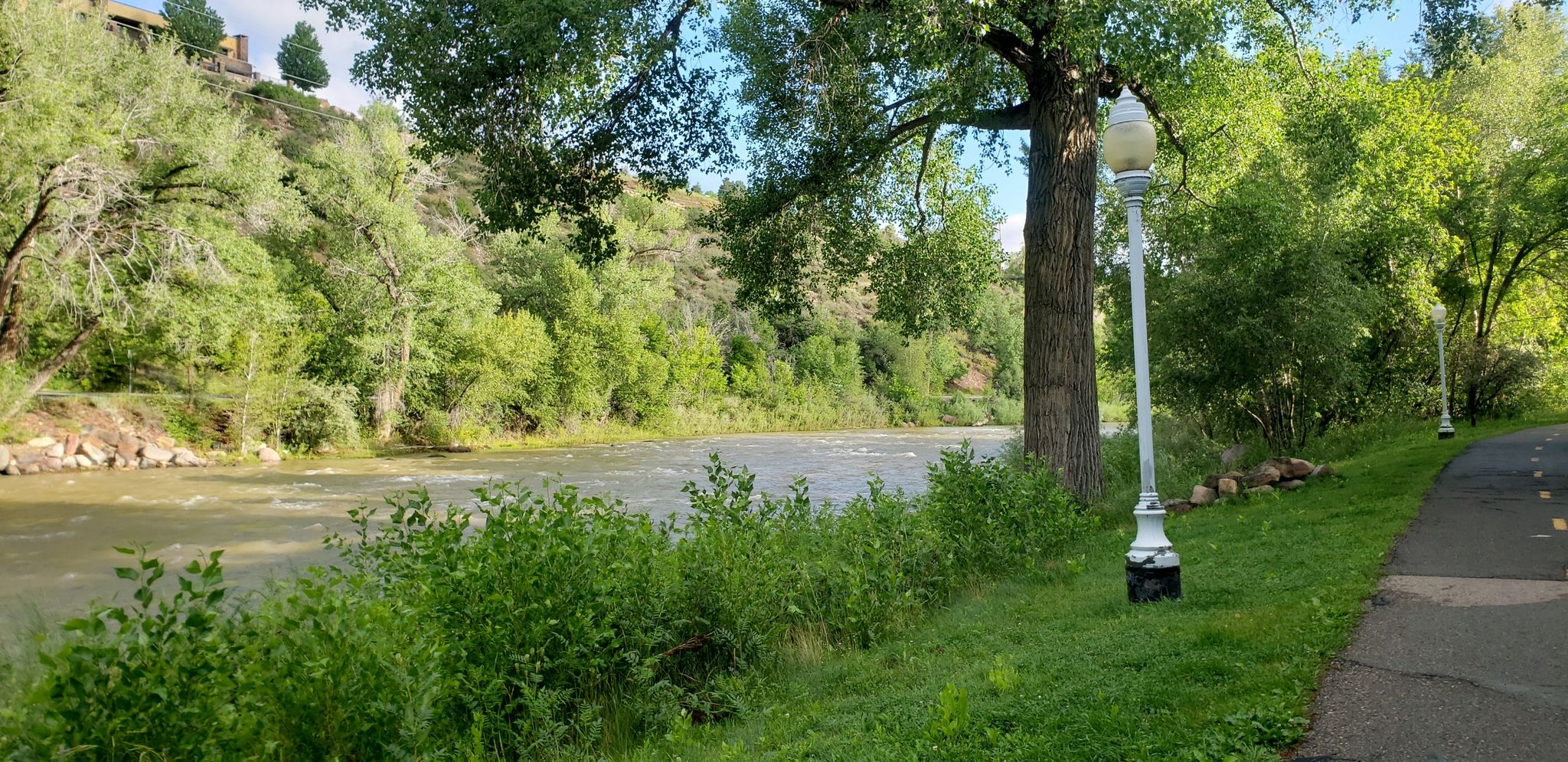 A paved path with lampposts runs alongside a flowing river and green trees. - Historic Downtown Durango – Animas River Trail loop from La Plata County