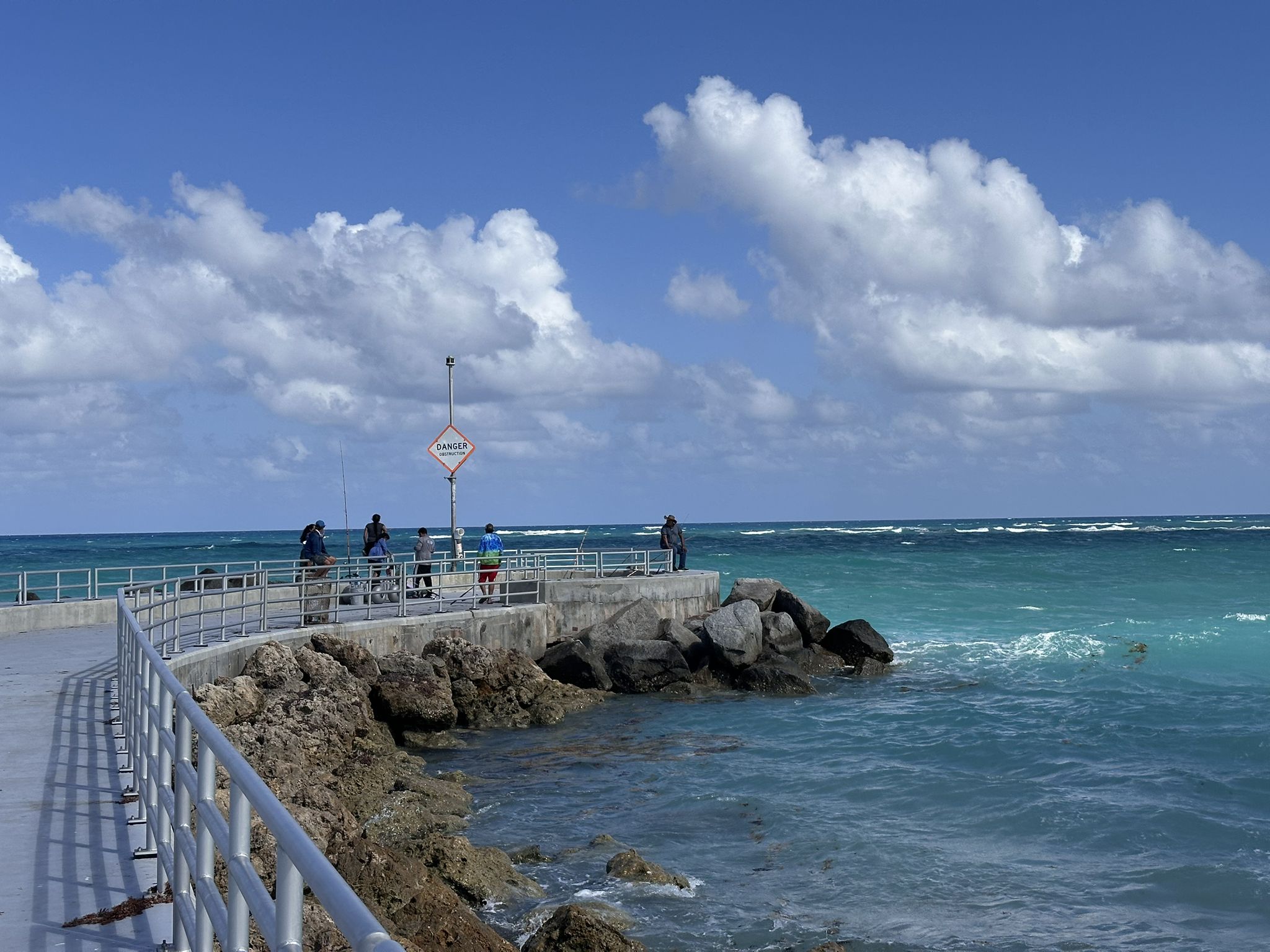 People fishing on a sunny pier next to turquoise ocean water under blue sky. - DuBois Park & Jupiter Beach Park loop
