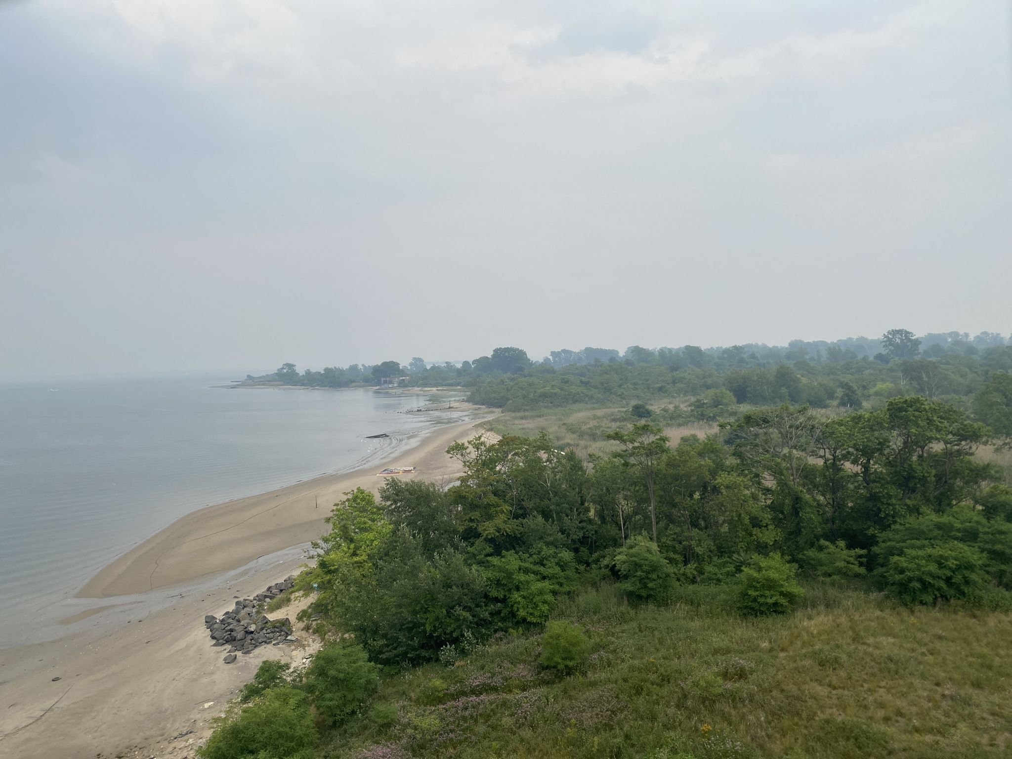 Sandy beach curving along a forested coastline under an overcast sky. - Jamaica Bay Greenway – Jamaica Bay Greenway loop from Euclid Avenue