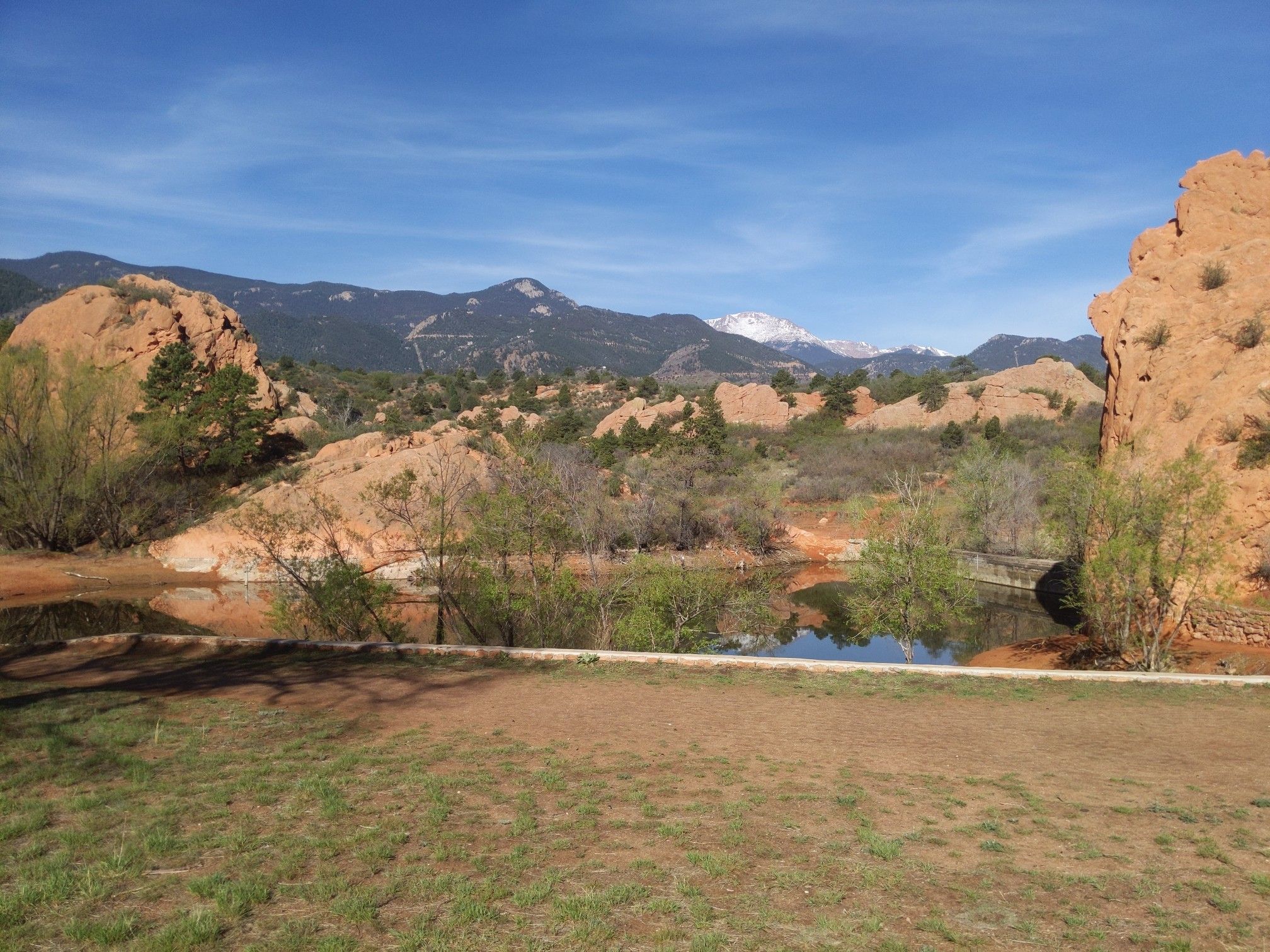 Calm lake reflecting red rocks and snow-capped mountains under blue sky. - Red Rock Canyon Open Space – Red Rock Canyon Ponds loop from Old Colorado City