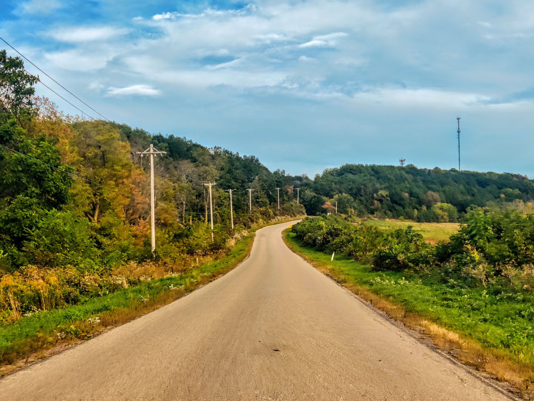 A winding road through green and autumn trees under a bright, cloudy sky. - Devil's Lake State Park – Devil's Lake State Park loop from Parfrey's Glen State Natural Area