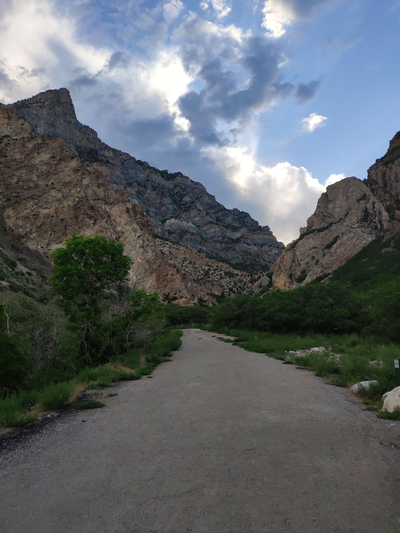 A paved path leads through a canyon with rocky mountains under a cloudy sky. - Rock Canyon Cave via Rock Canyon Trail