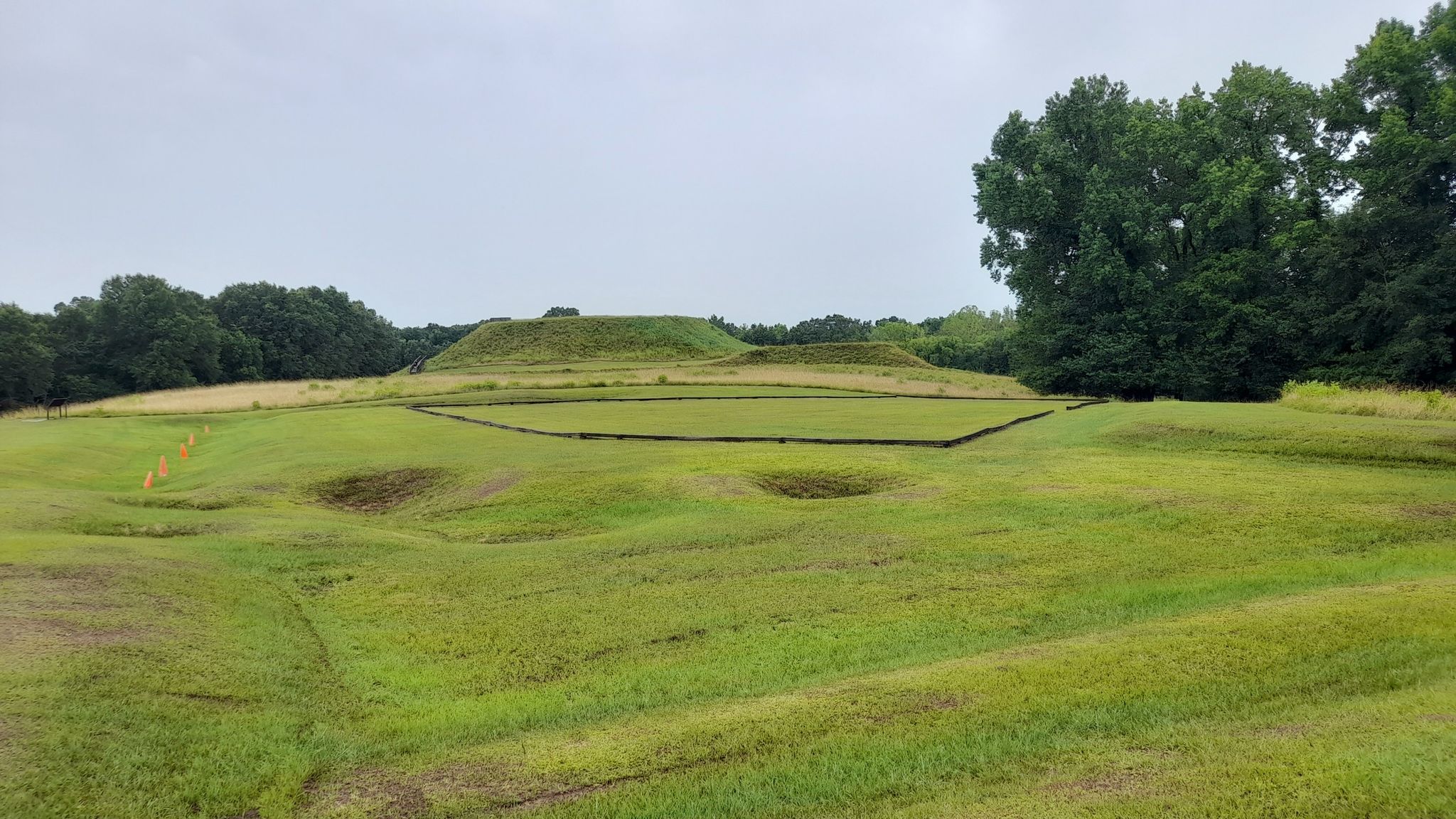 Green grassy mounds and depressions under an overcast sky, distant trees. - Great Temple Mound loop from Ocmulgee Mounds National Historical Park