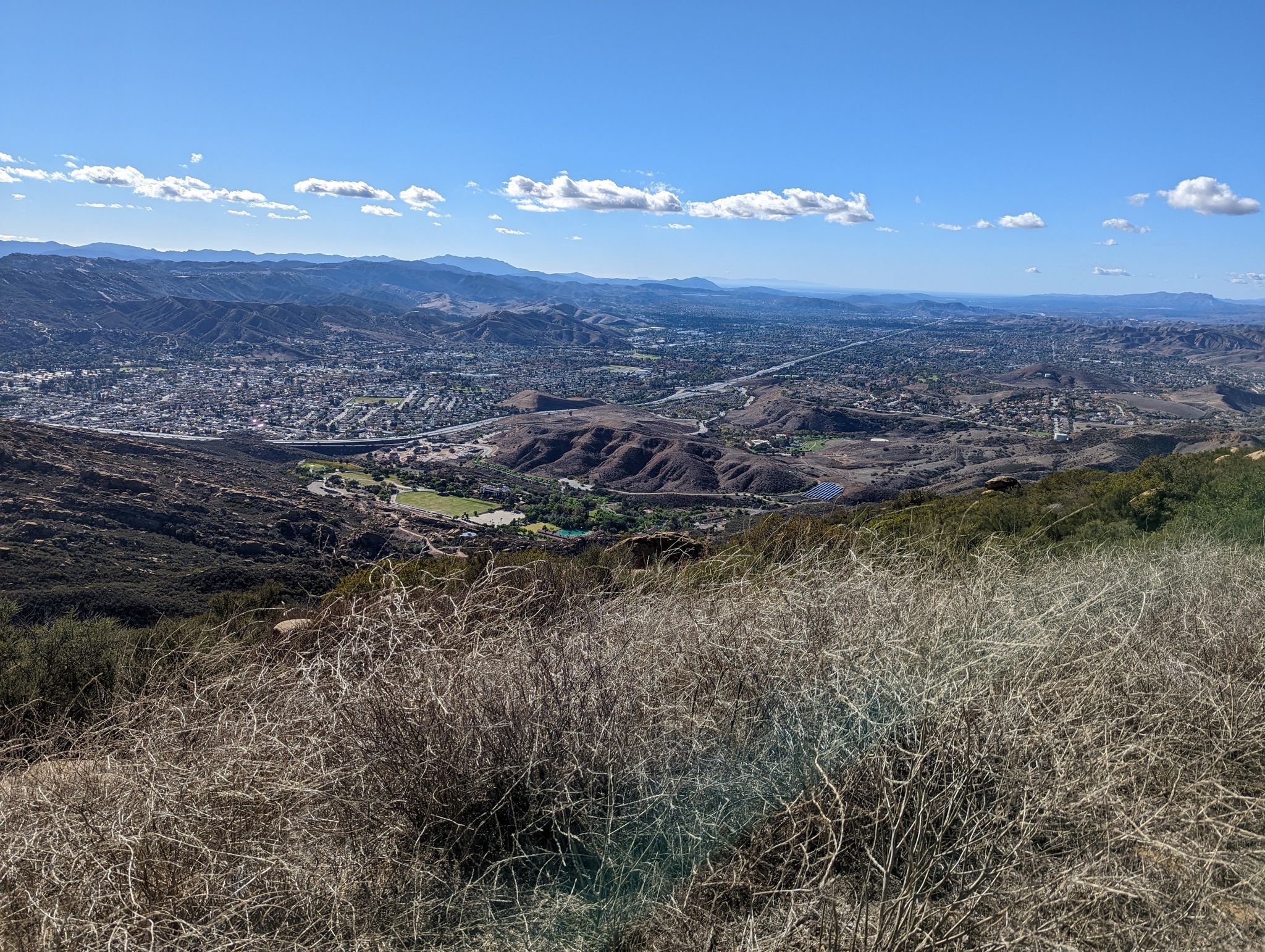 Wide view of a valley with a town and green fields under a blue sky. - Corriganville Park Picnic Area – Rocky Peak Trail loop from Santa Susana
