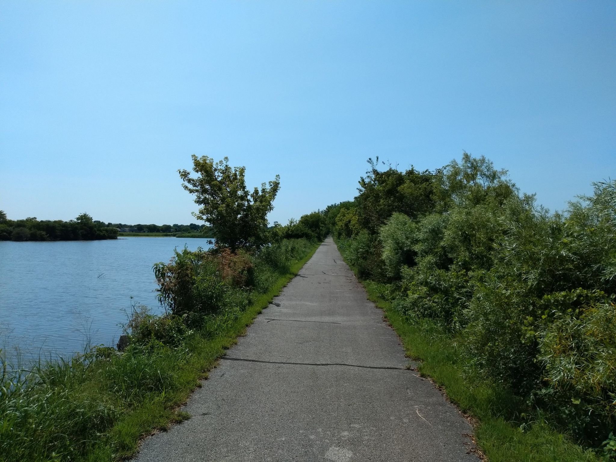 A paved path alongside a wide blue lake under a clear sky. - Downtown Flossmoor – Old Plank Road Trail loop from Flossmoor
