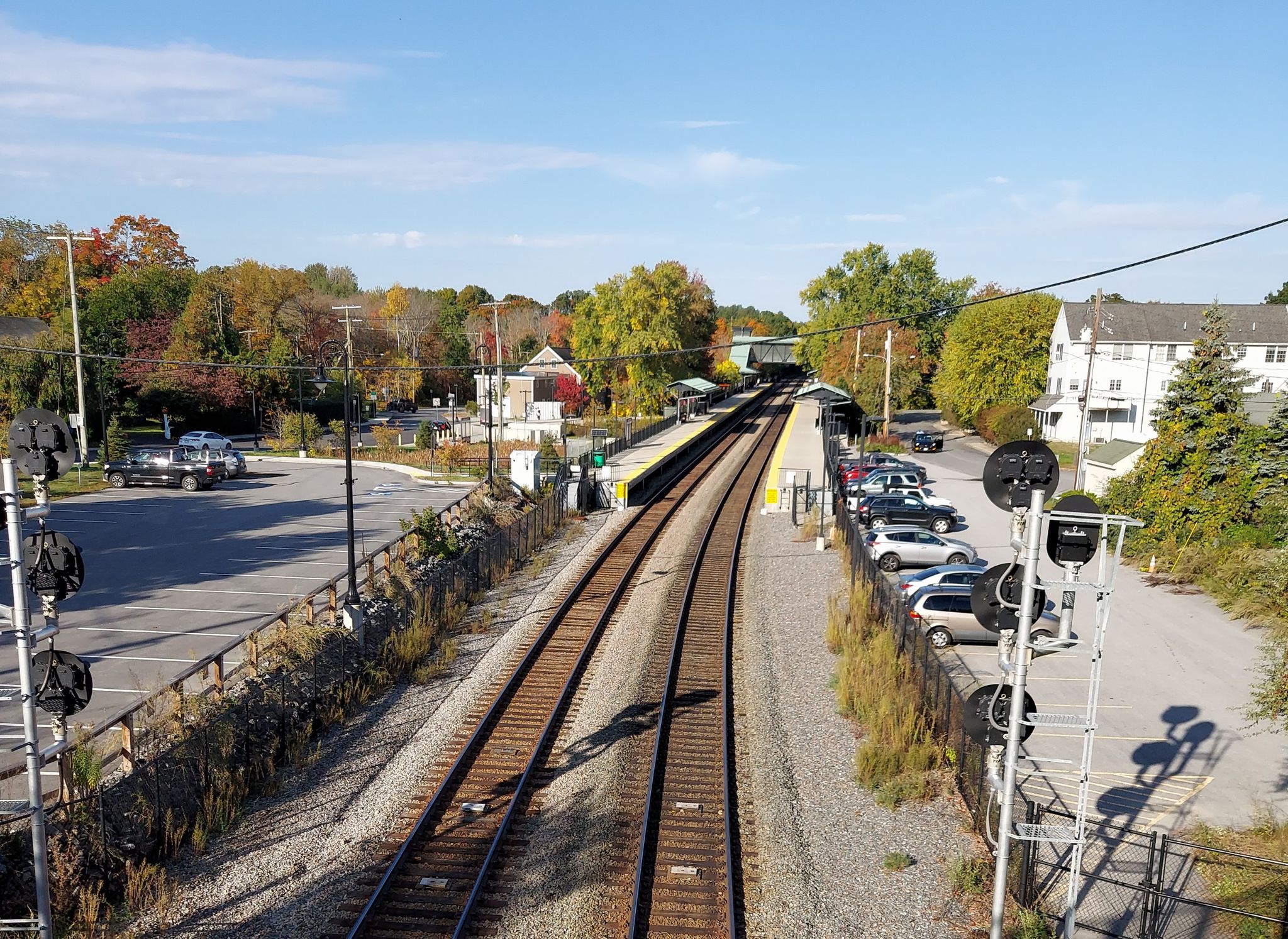 Train tracks leading to a station platform, surrounded by autumn trees and buildings. - Mill Pond Footbridge and View loop from Caouette-Simeone Conservation Restriction