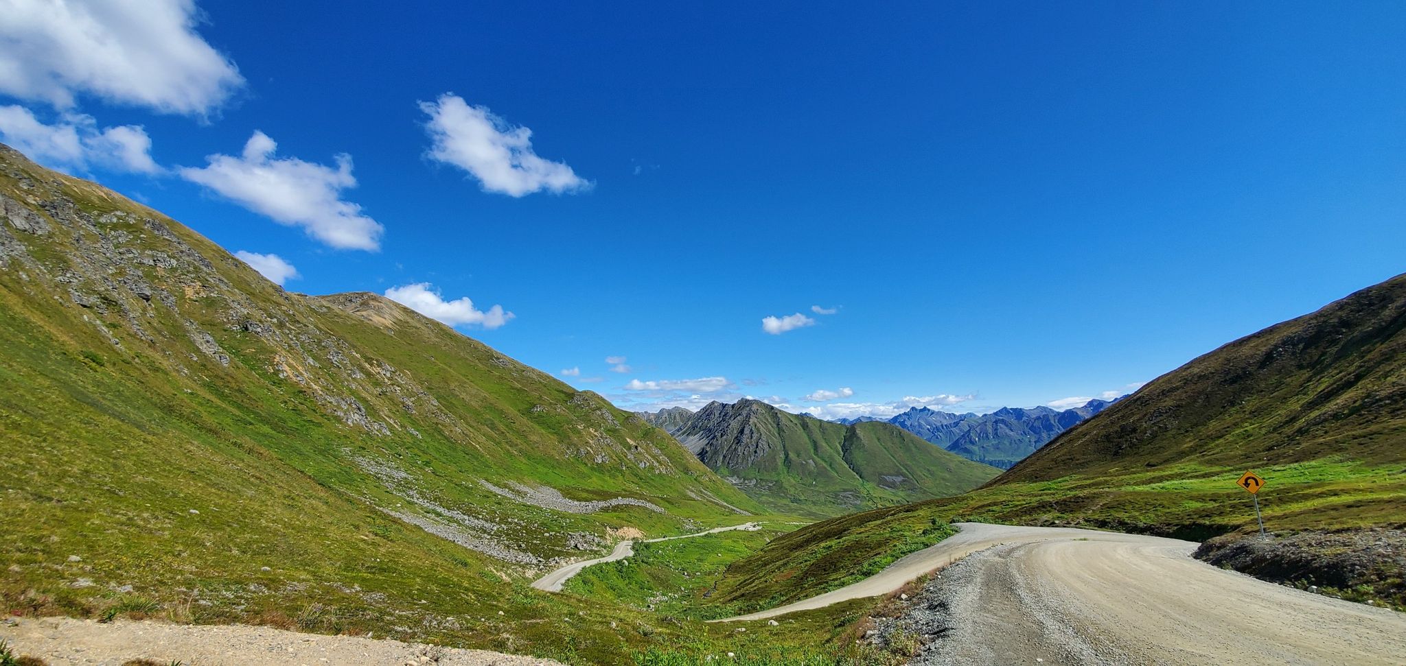 Sunny mountain valley with a winding dirt road under a blue sky. - Hatcher Pass Scenic Drive