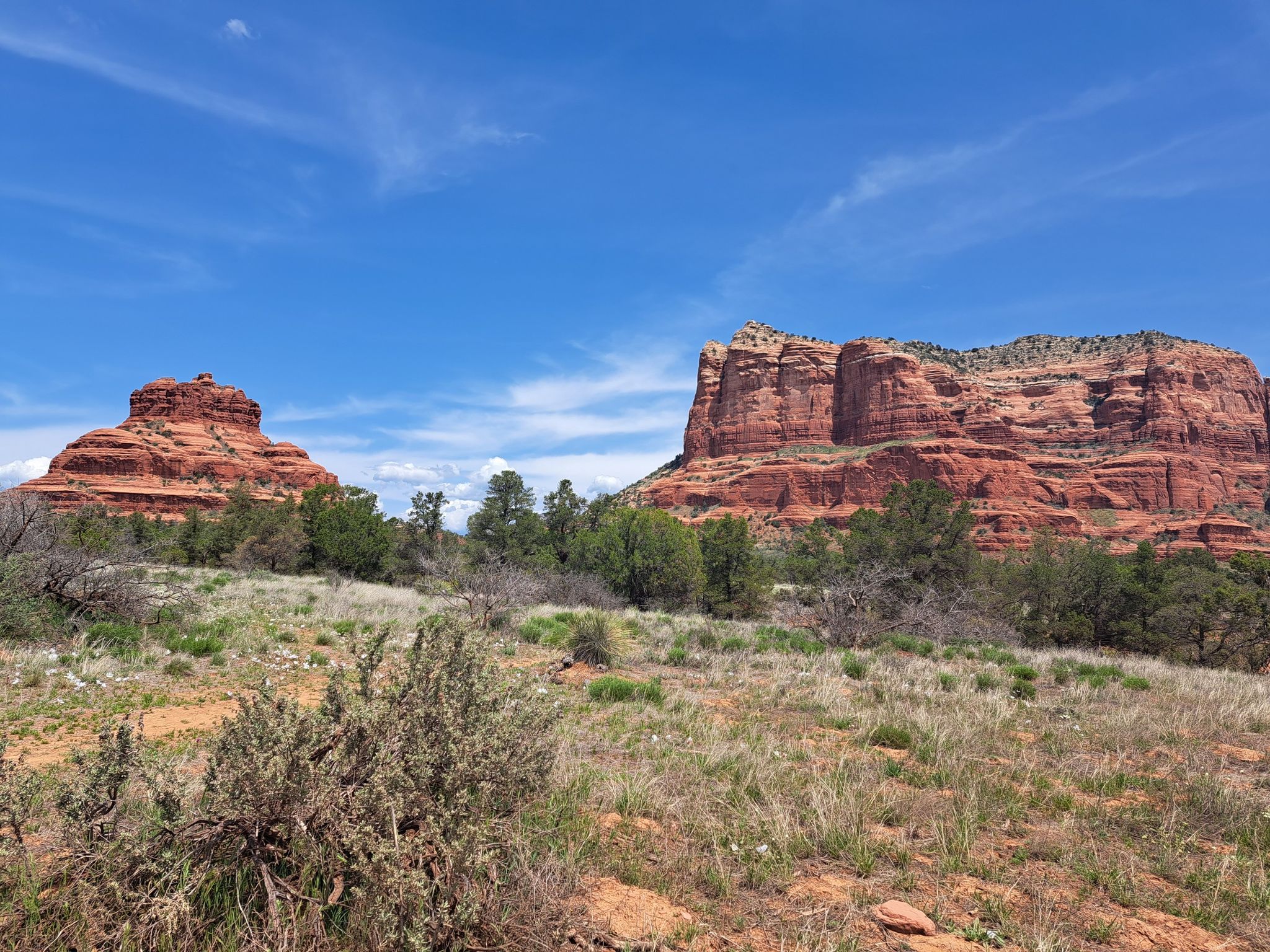 Two distinct red rock formations under a bright blue sky, with green shrubs. - Bell Rock Trail
