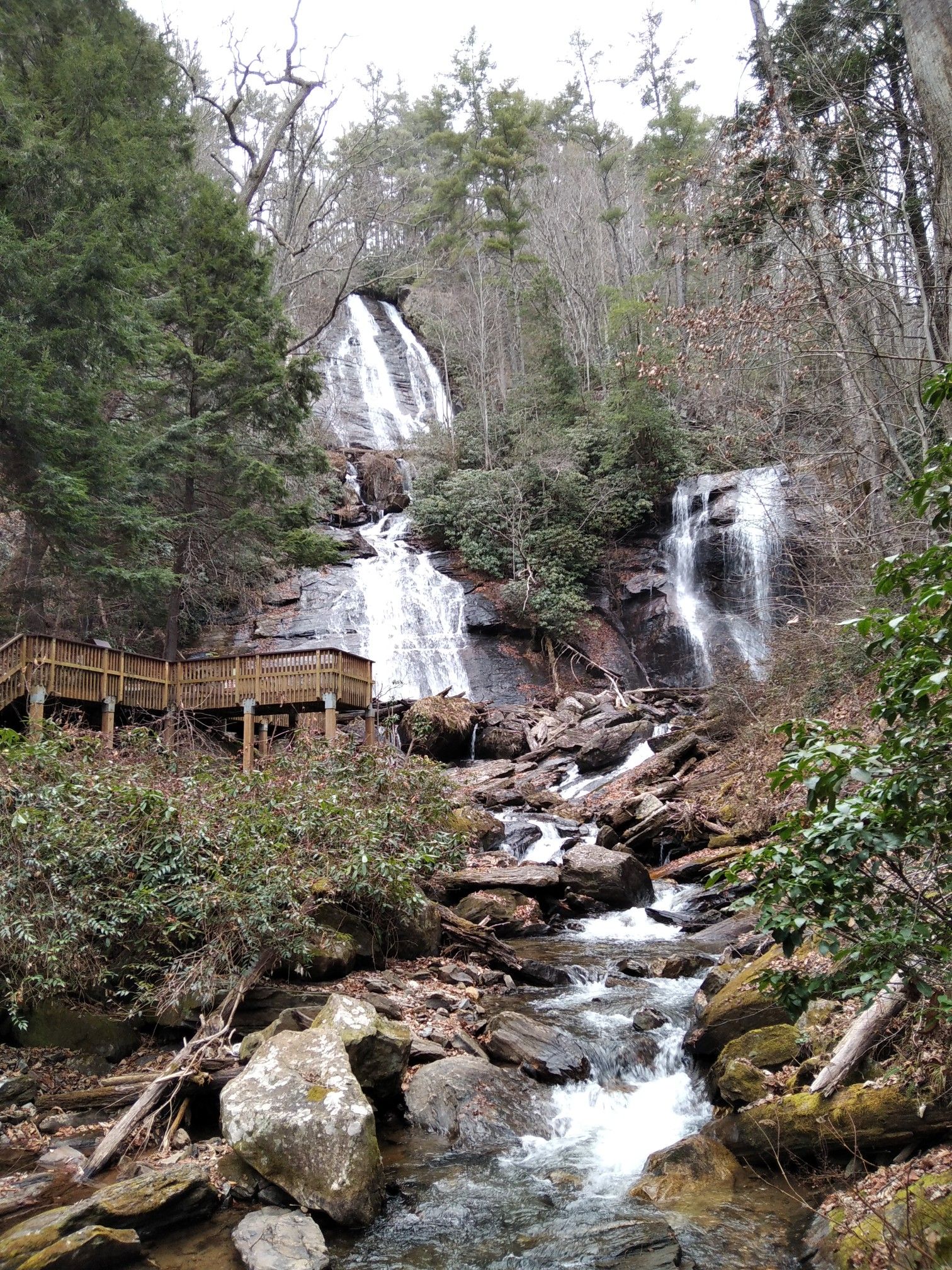 Multiple waterfalls cascade down a rocky, forested slope with a wooden walkway. - Smith Creek Trail to Anna Ruby Falls