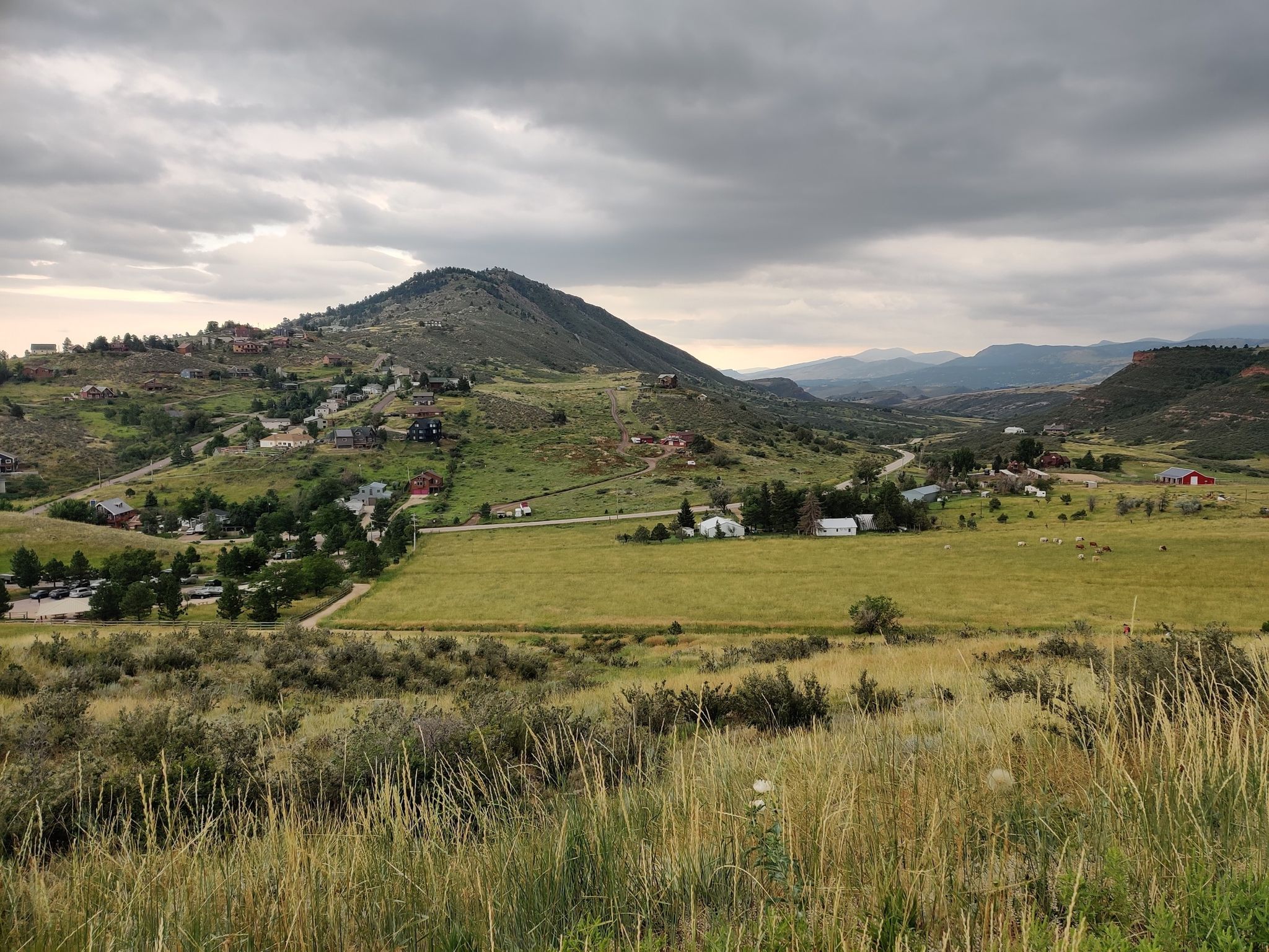 Cloudy day over a green valley with scattered houses and a distant mountain. - Hiking loop from Horsetooth Mountain Open Space