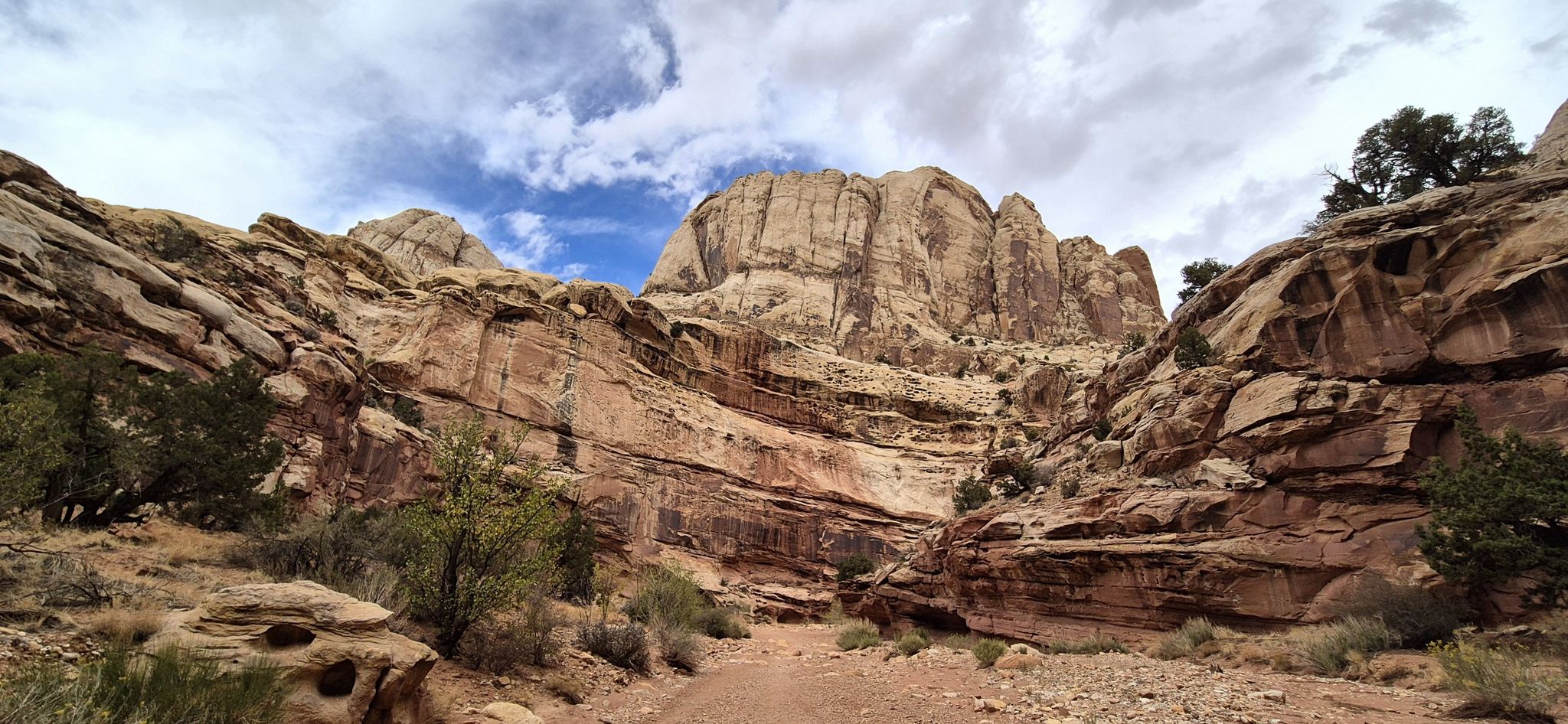 Majestic canyon walls with layered rock formations under a partly cloudy sky. - Grand Wash Trail