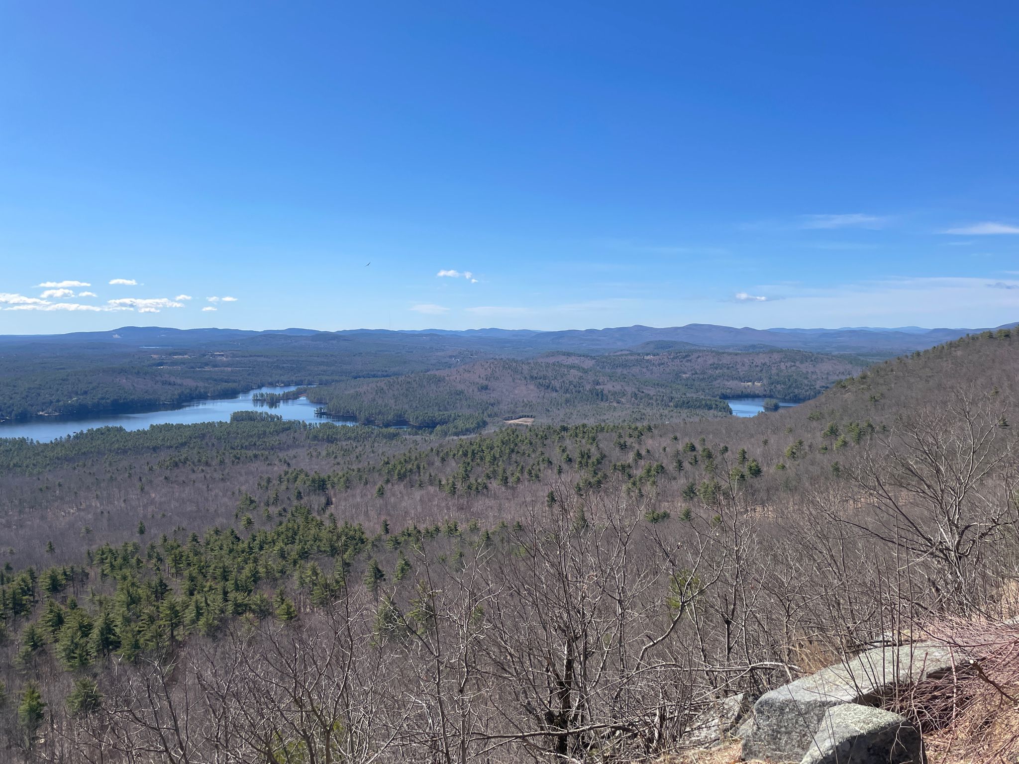 Expansive view of lakes, forests, and distant mountains under a clear blue sky. - Ledges Trail