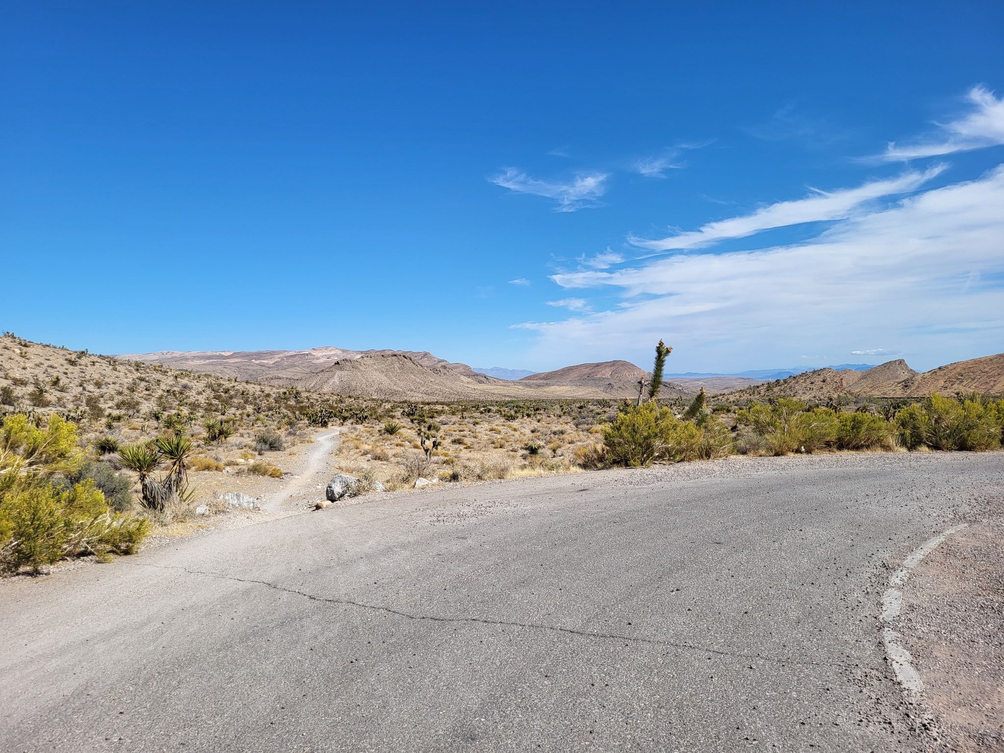 Paved road curves through a vast desert landscape with distant mountains. - The Hurl and Landmine Loop
