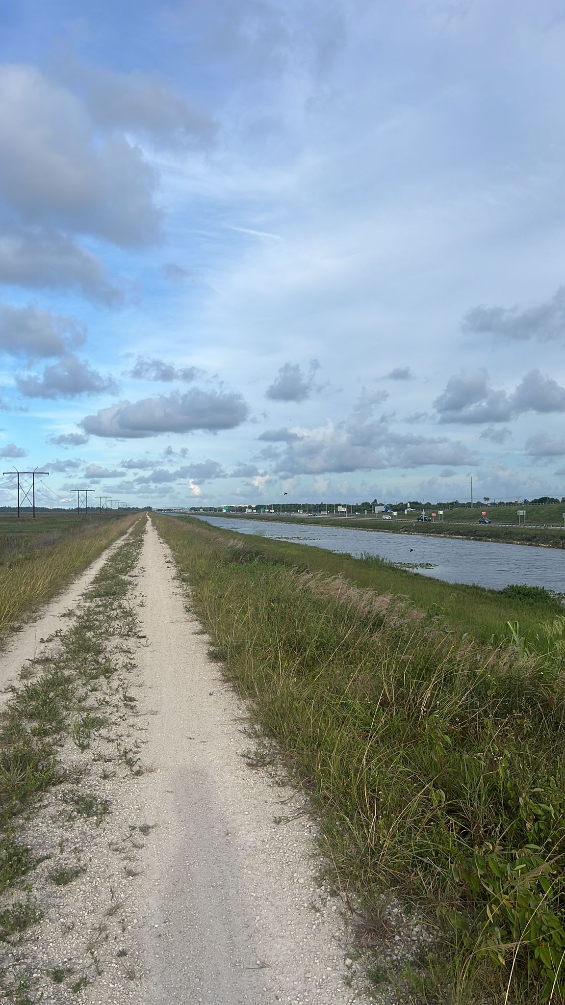 A long dirt road next to a canal under a cloudy sky. - Conservation Levee Greenway Loop