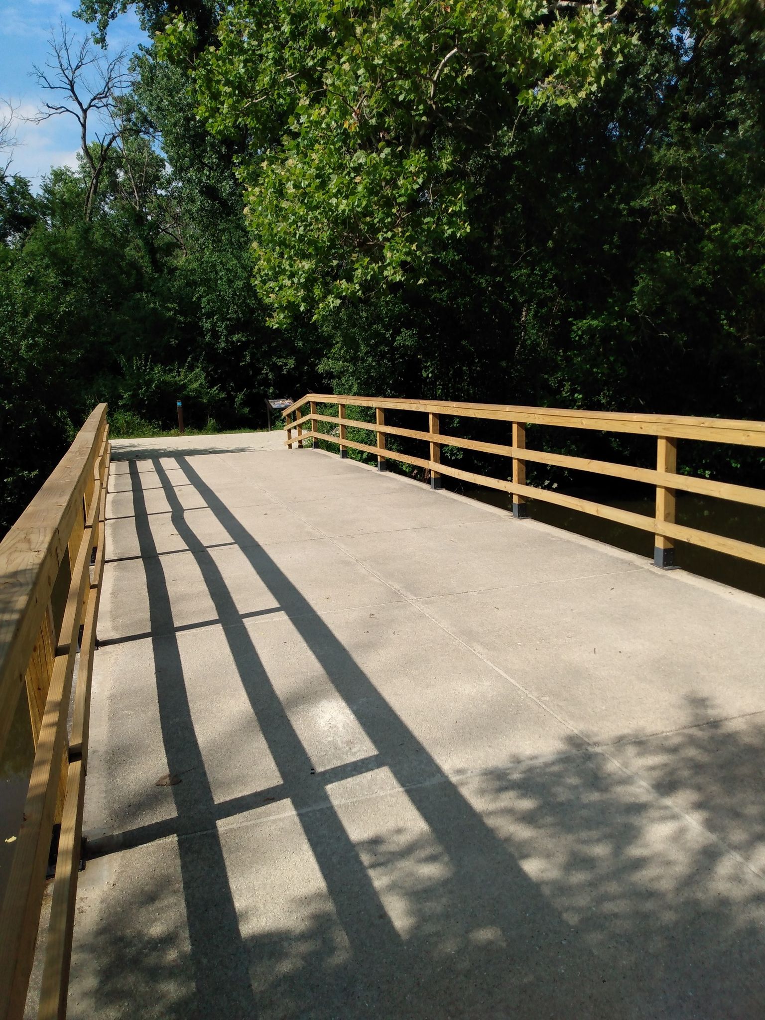 A concrete bridge with wooden railings, casting long shadows on a sunny day. - North Island loop from Oak Brook