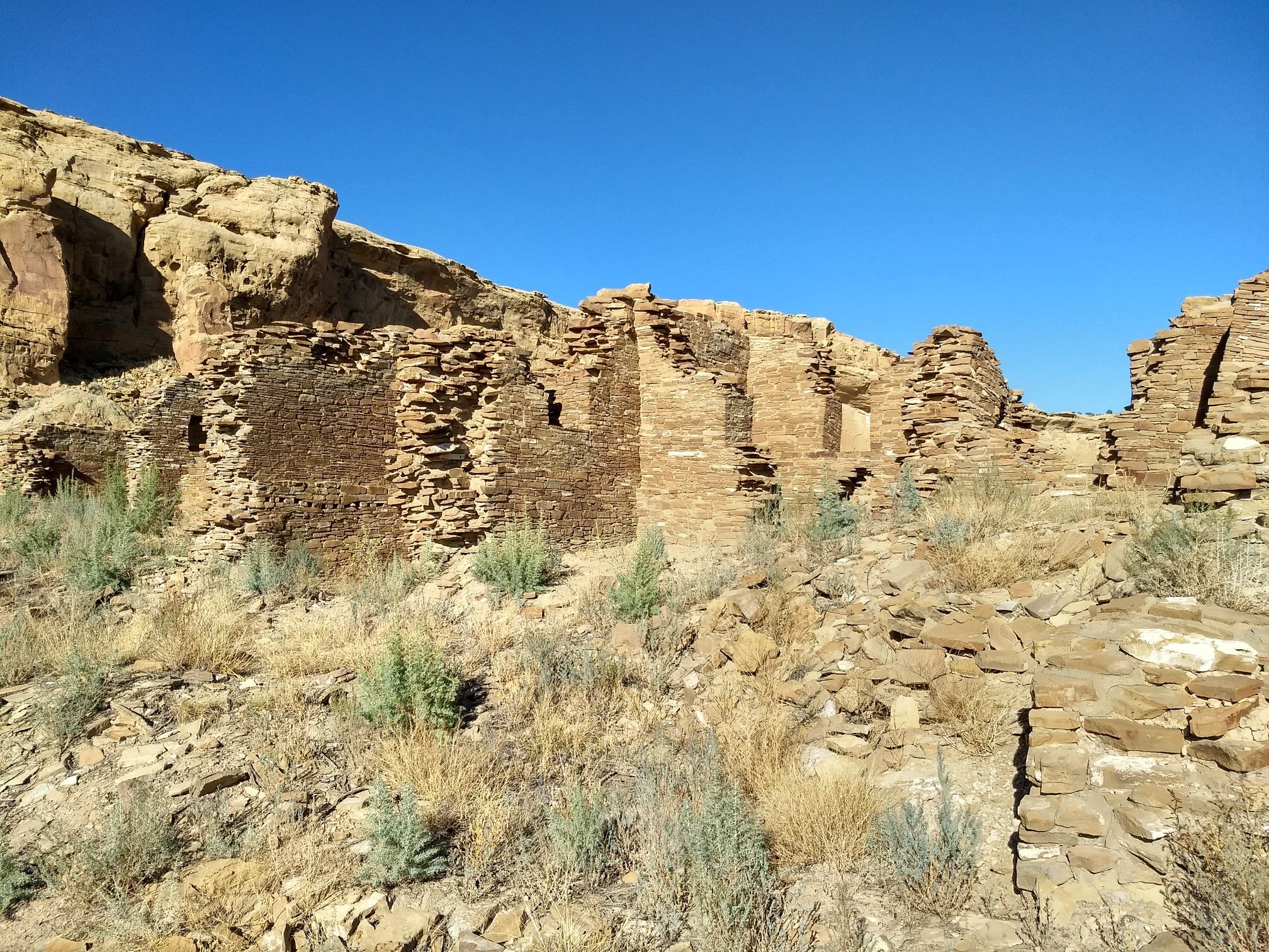 Extensive stone ruins built into a desert cliffside, clear sky. - Wijiji Trail