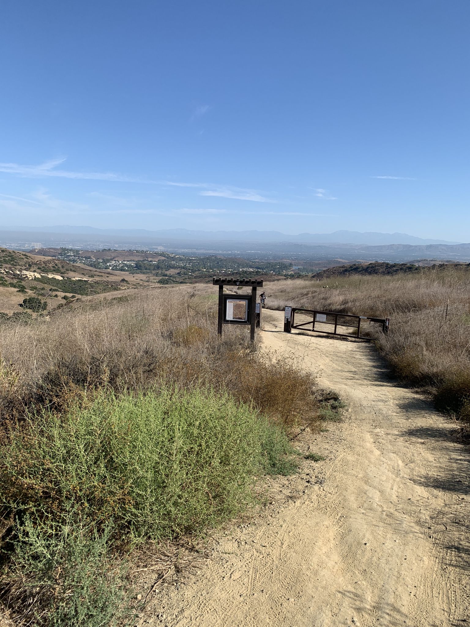 Dirt path leading to a closed gate and sign, overlooking a valley. - Bommer Ridge, Lizard, and Laurel Canyon Loop