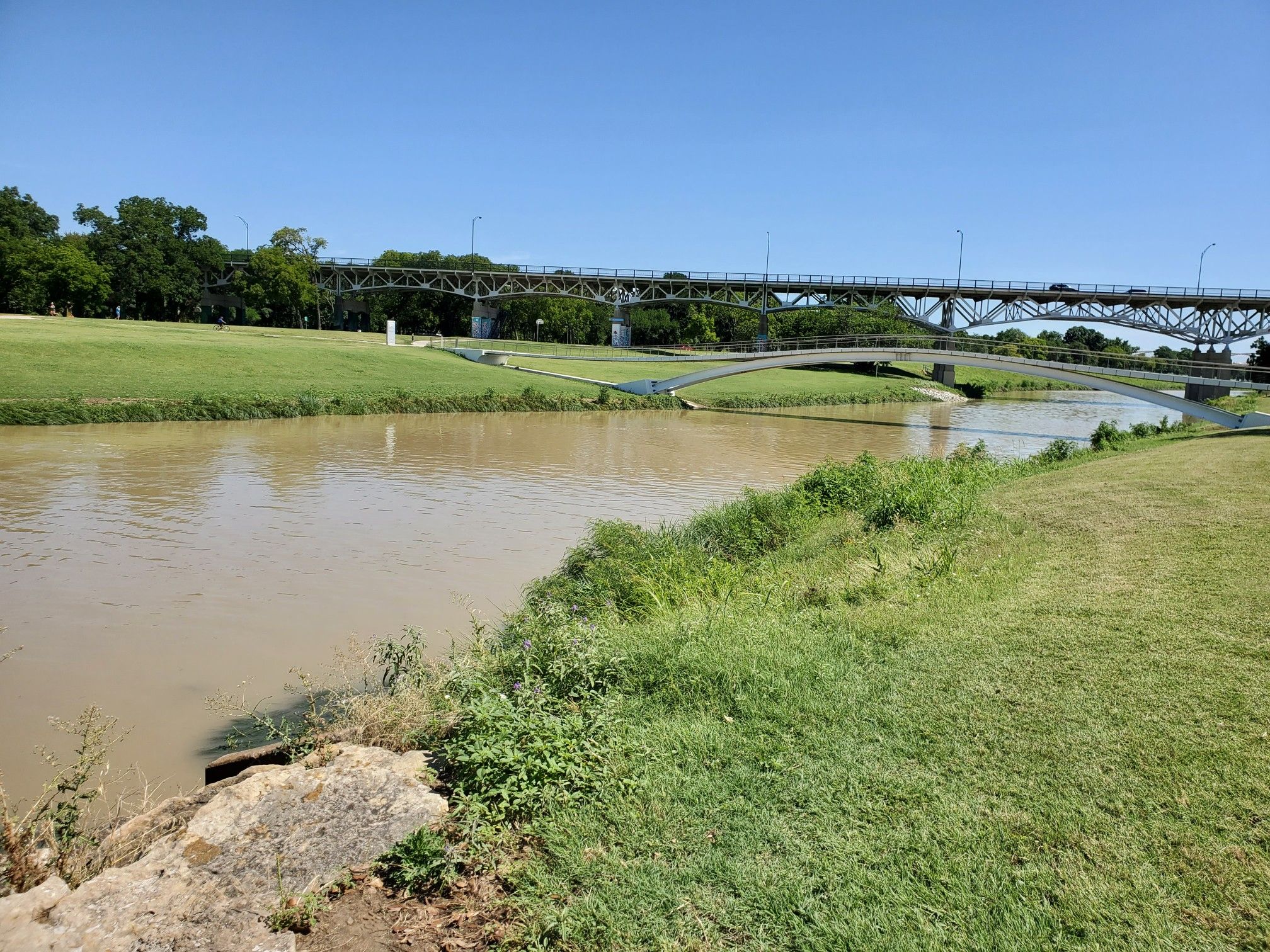 A wide muddy river flows under two bridges on a sunny day. - Trinity Trails