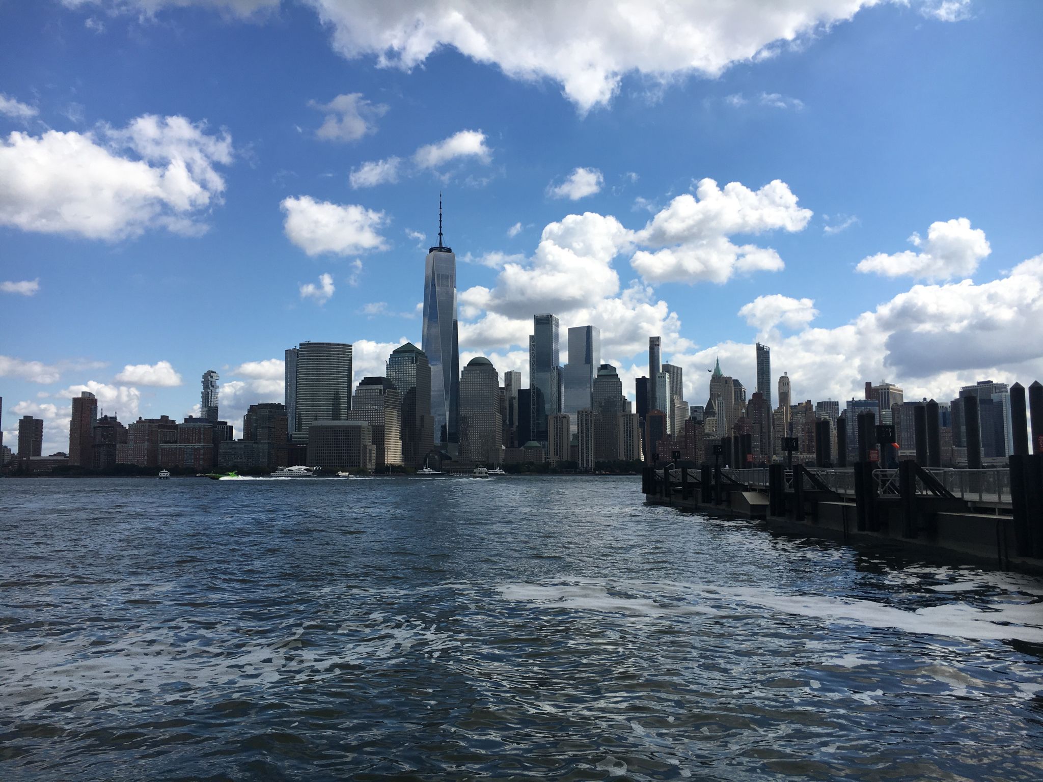 City skyline viewed from choppy water under a bright blue sky with clouds. - Liberty Landing Marina – Jersey City 9/11 Memorial loop from Jersey City