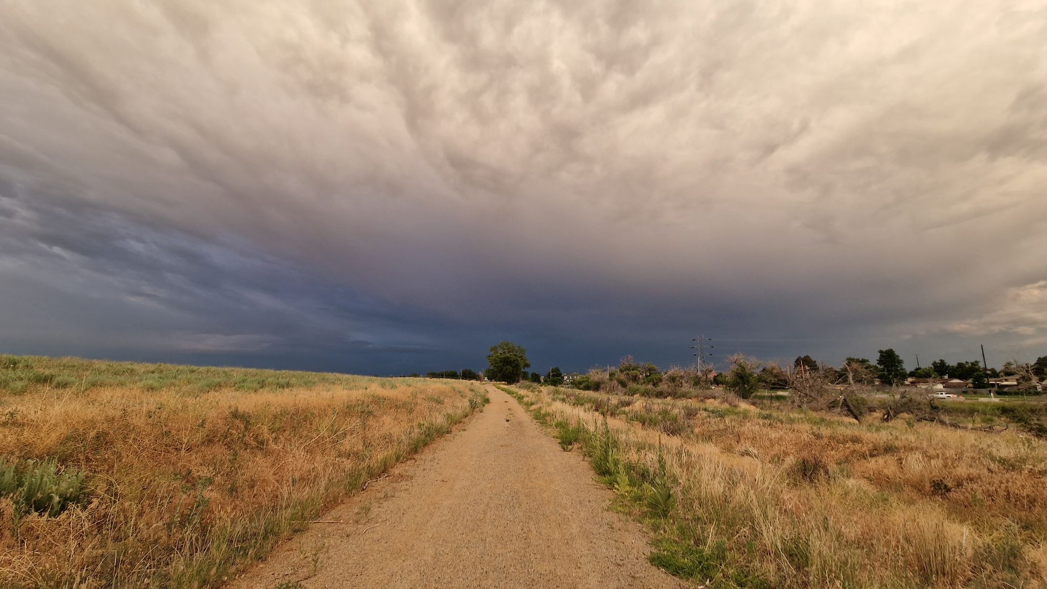 Dirt path through dry grass under a dark, stormy sky. - Rod and Gun Club Pond loop from Dick's Sporting Goods Park
