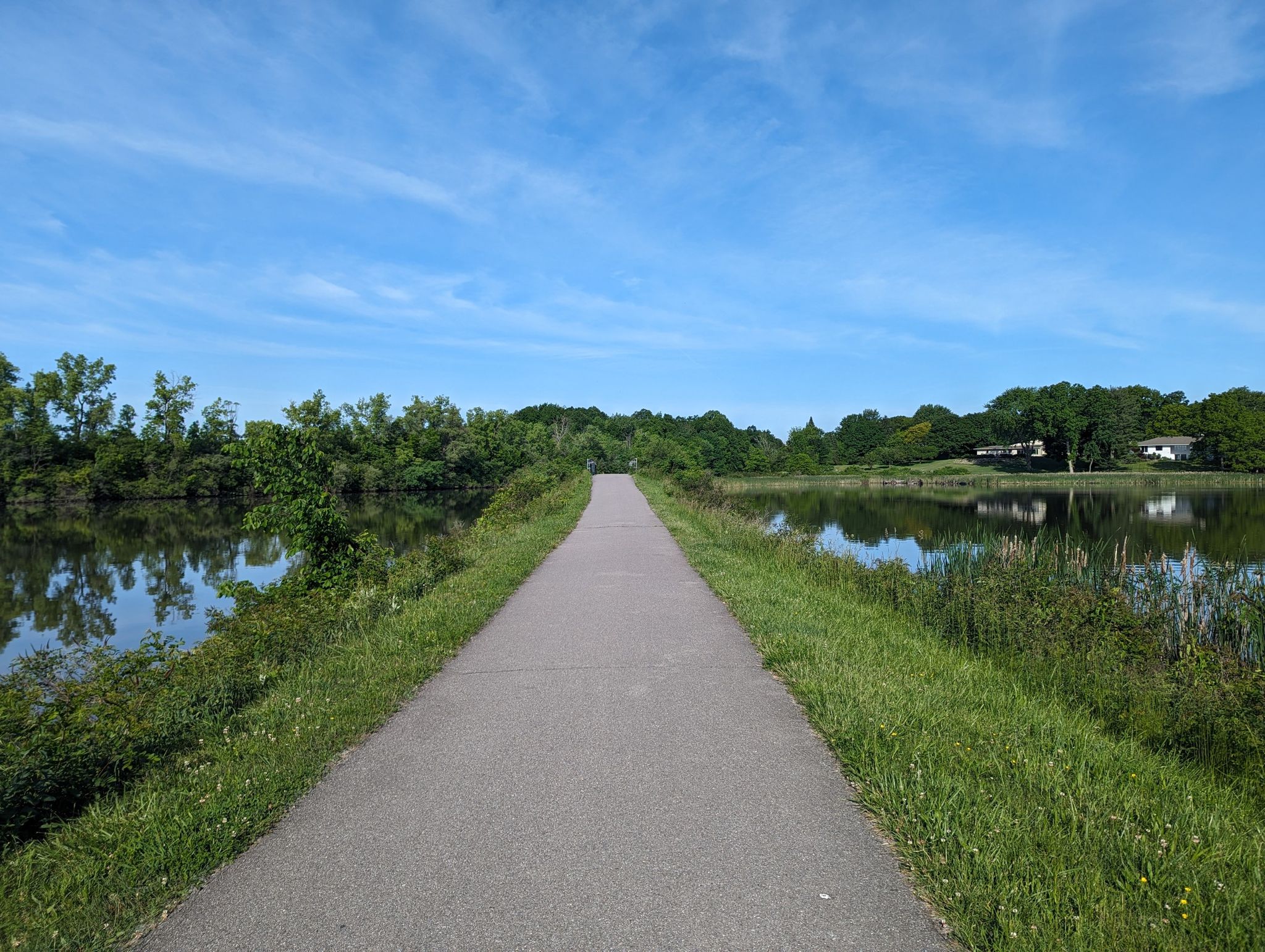 Paved path between two calm bodies of water, surrounded by green foliage. - Erie Canalway and Genesee Riverway Trail Loop