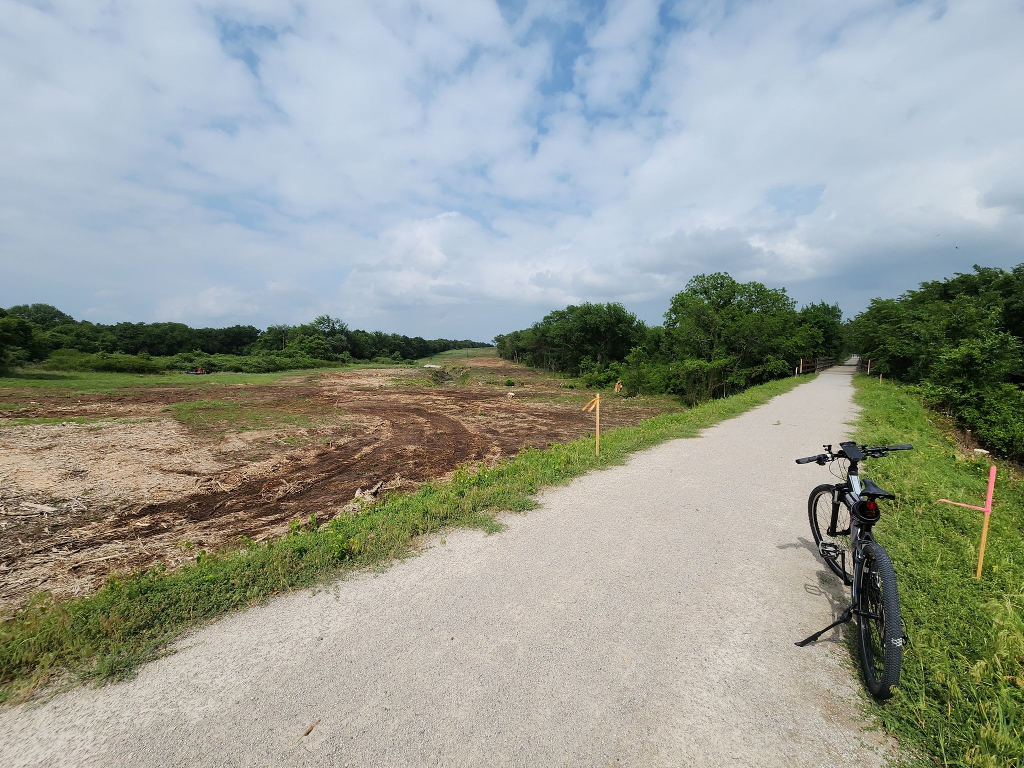 A bicycle parked on a dirt path next to cleared land and green trees. - Lake Mineral Wells State Trailway