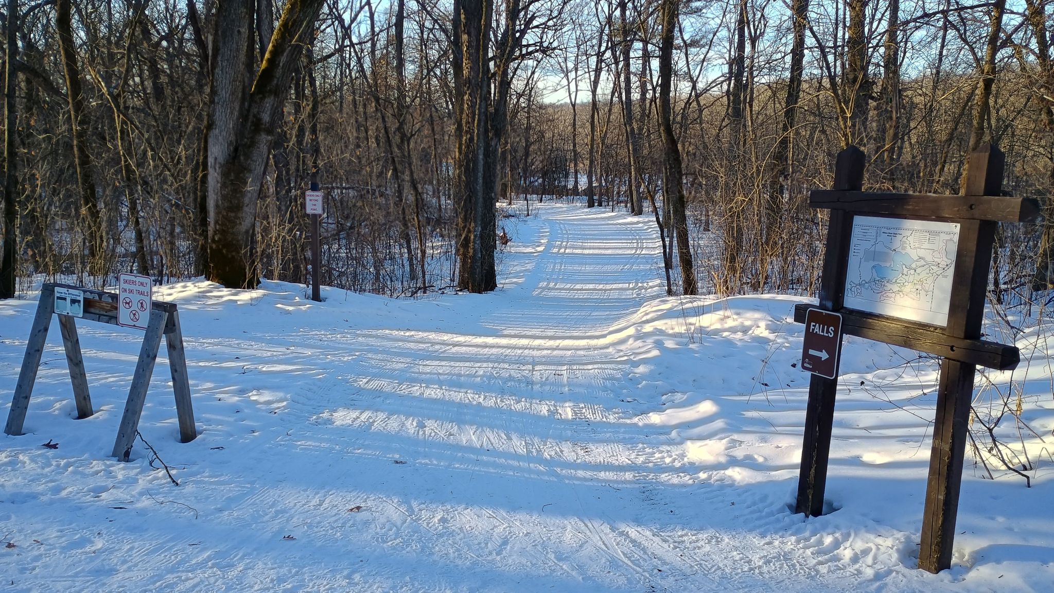 A snowy forest path with informational signs under bright winter sun. - Pioneer Trail