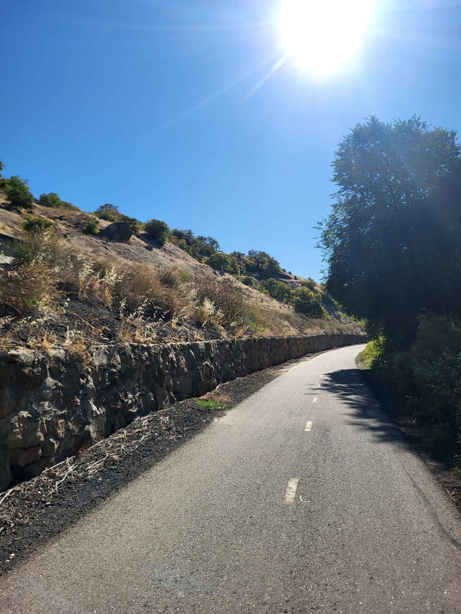 A paved path winds alongside a rocky hillside under a bright sunny sky. - Boise River Greenbelt – Boise River Greenbelt loop from Peace Valley Overlook Reserve
