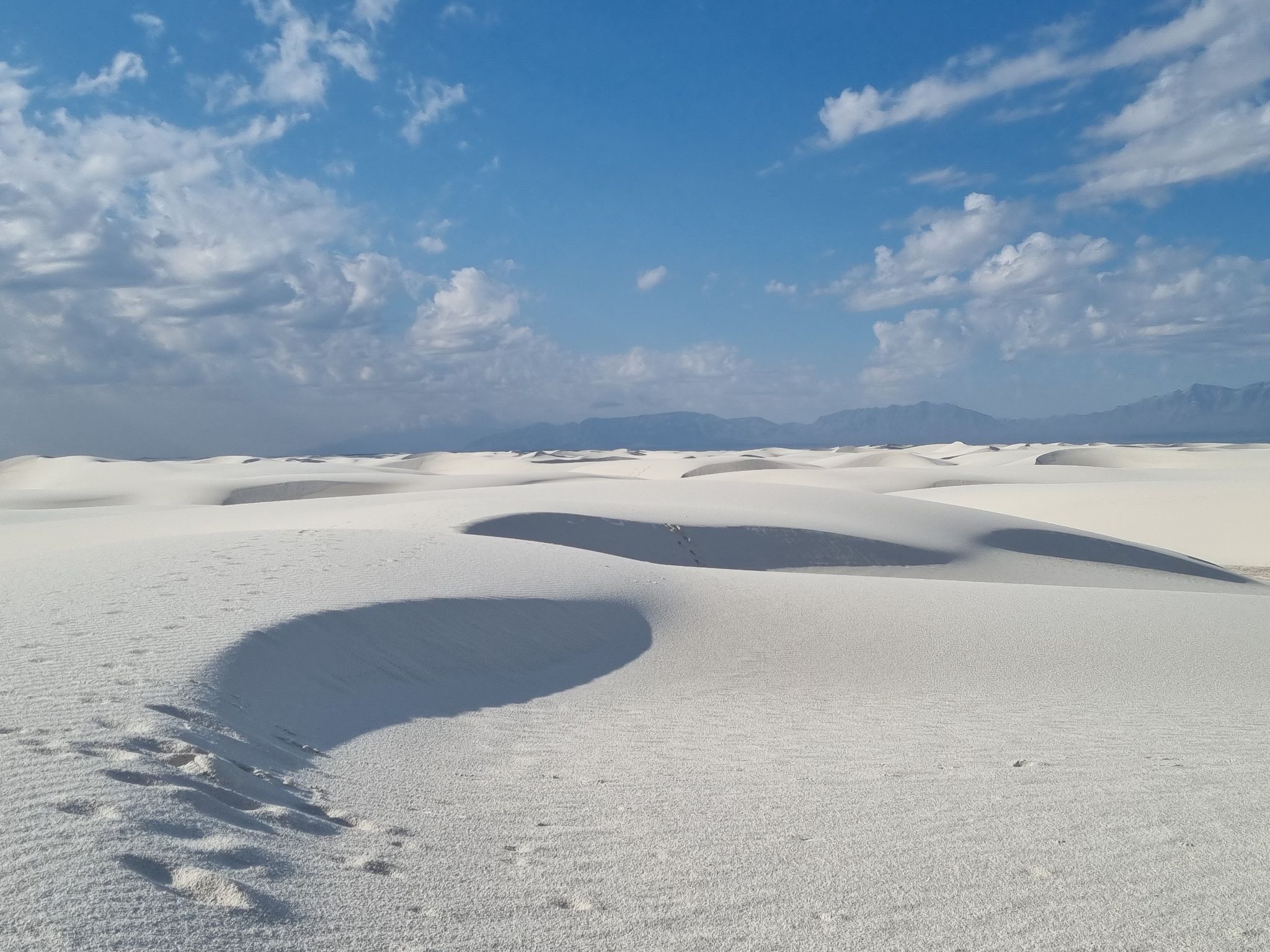 Bright white sand dunes with footprints under a blue sky with clouds. - Alkali Flat Trail