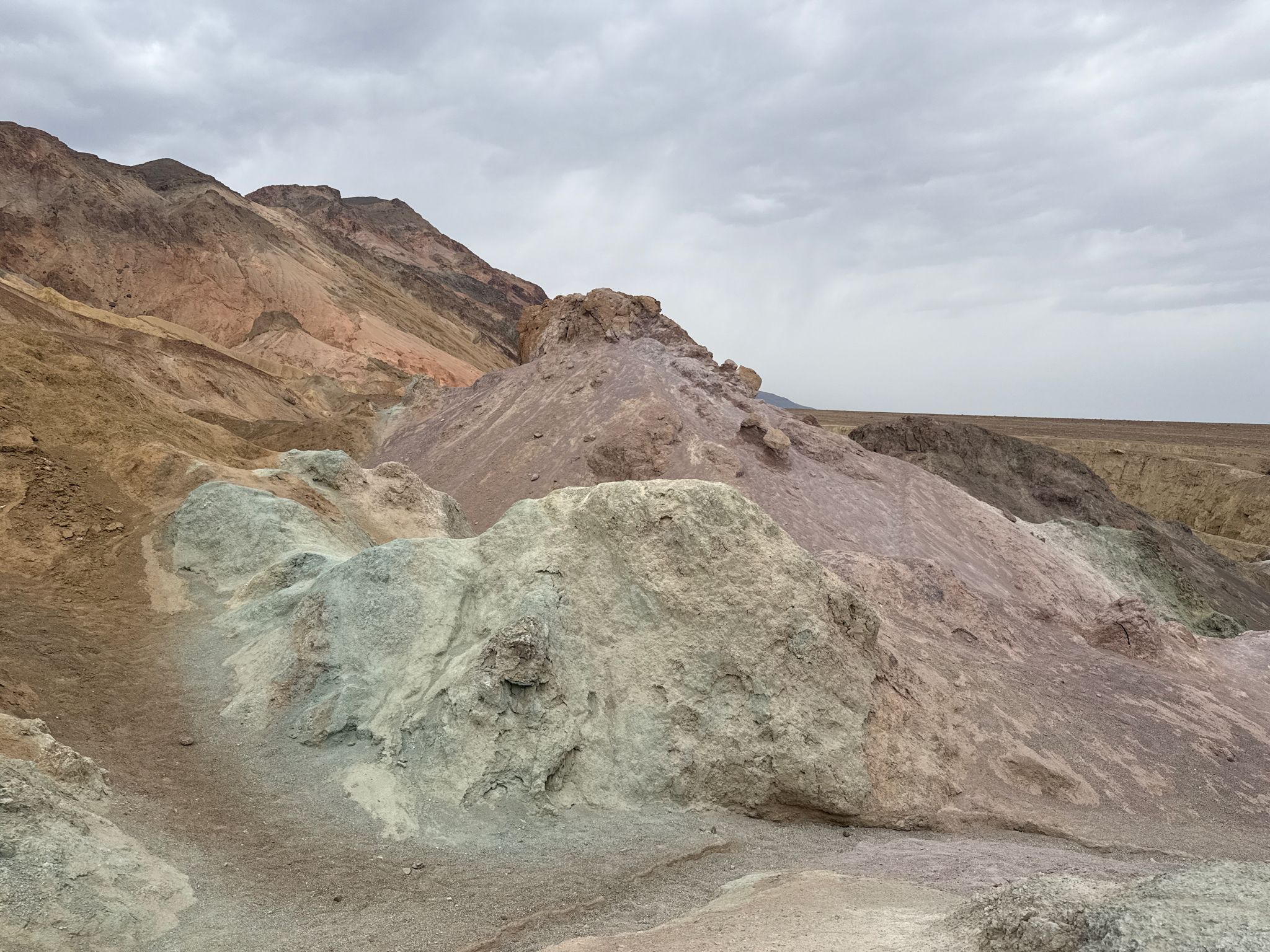 Multi-colored rock formations and hills under a cloudy, diffused sky. - Artists Palette Trail