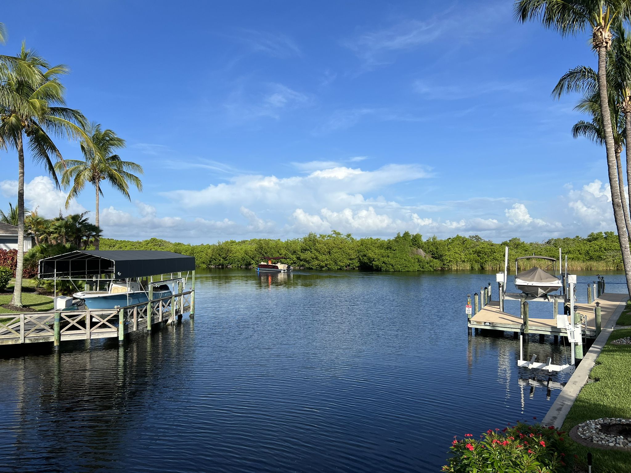 A calm canal with boat docks and lush green vegetation under a bright blue sky. - Progress Canal – Progress Canal loop from Cape Coral