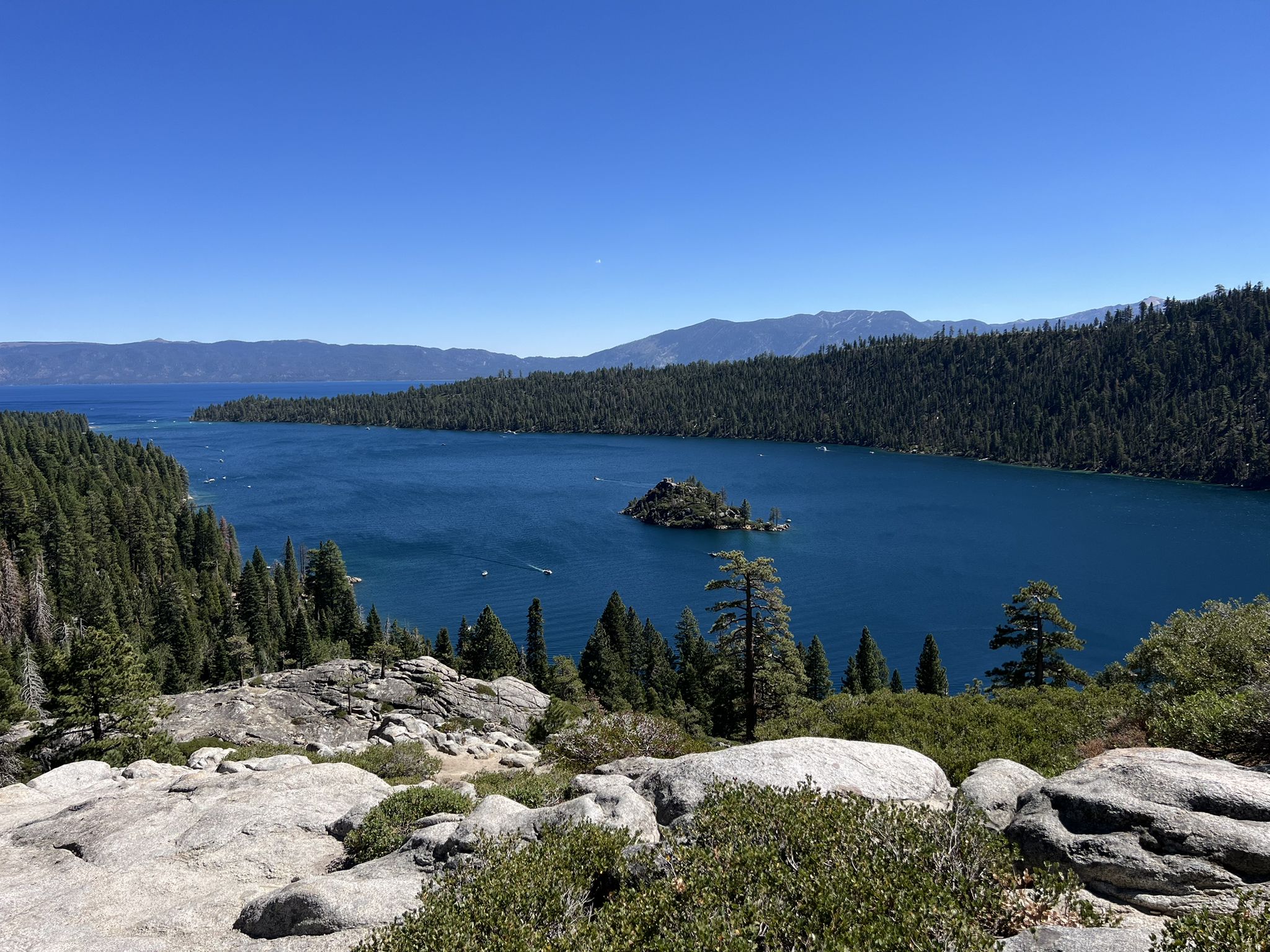 Wide view of a blue lake with a small island, surrounded by green forests. - Eagle Falls Trail
