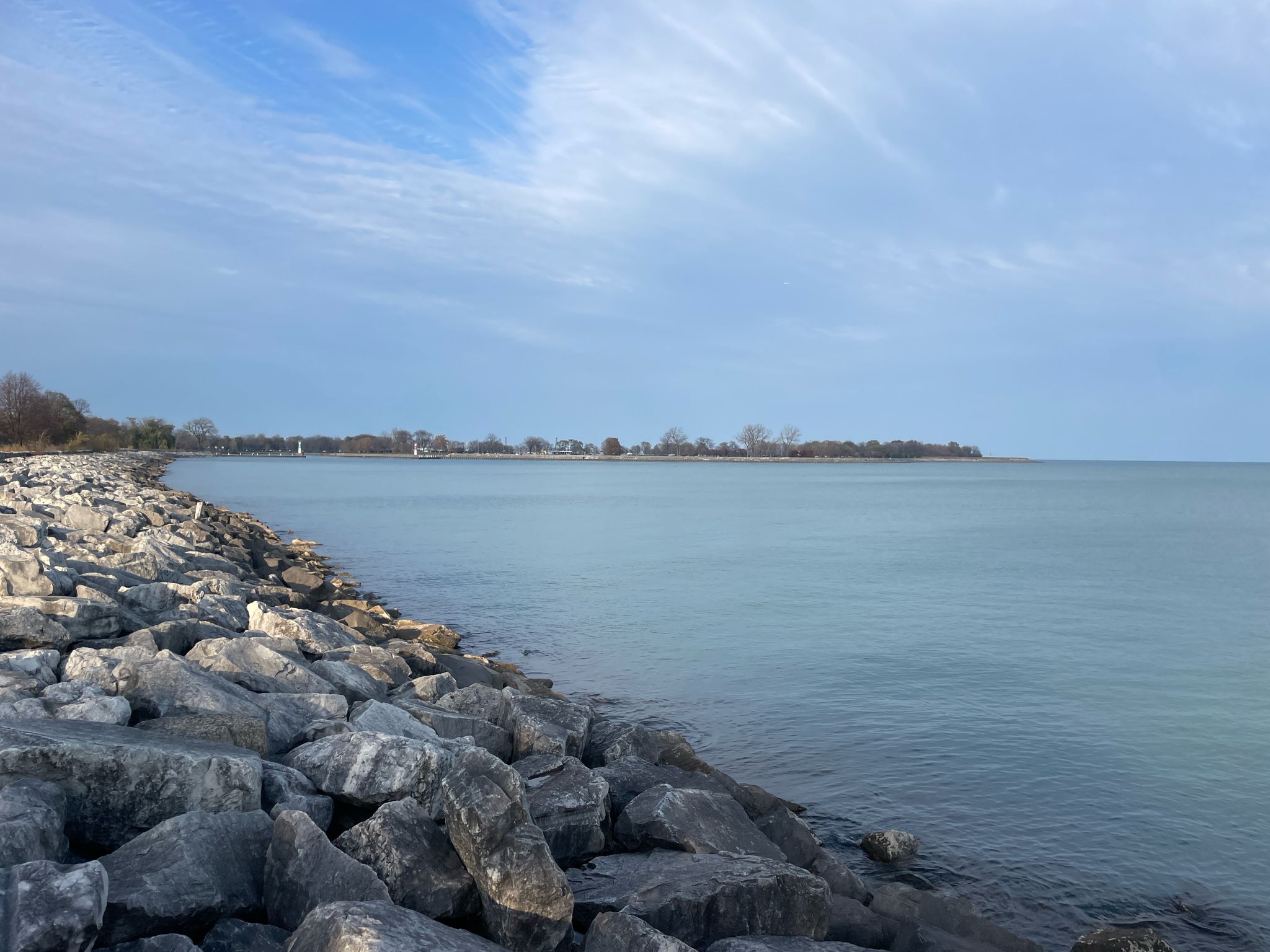 Rocky shoreline next to calm water under a partly cloudy sky. - Montrose Harbor Trail