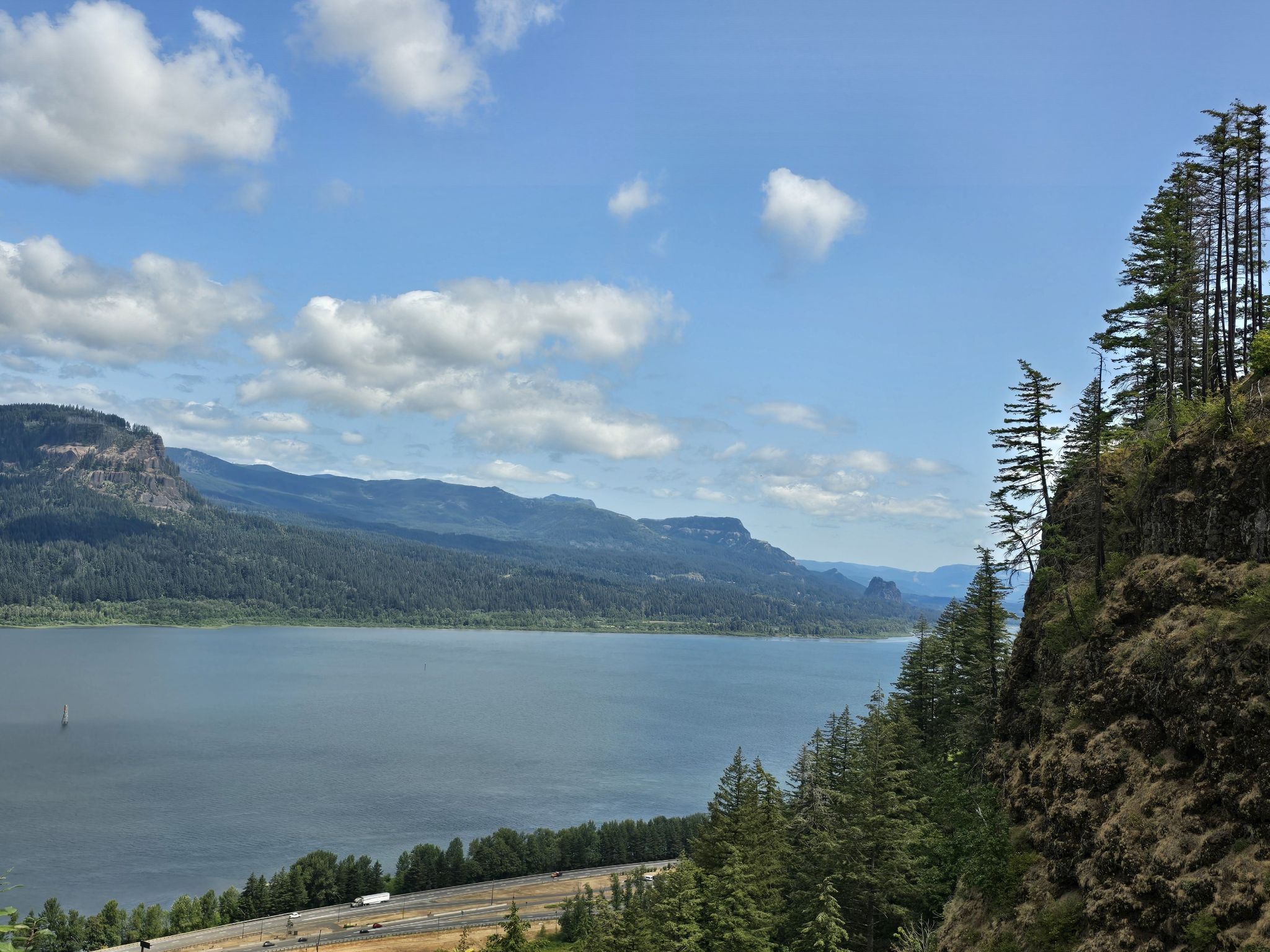 A wide river flows between forested mountains under a bright, cloudy sky. - Wahkeena Falls to Devils Rest and Angels Rest Loop