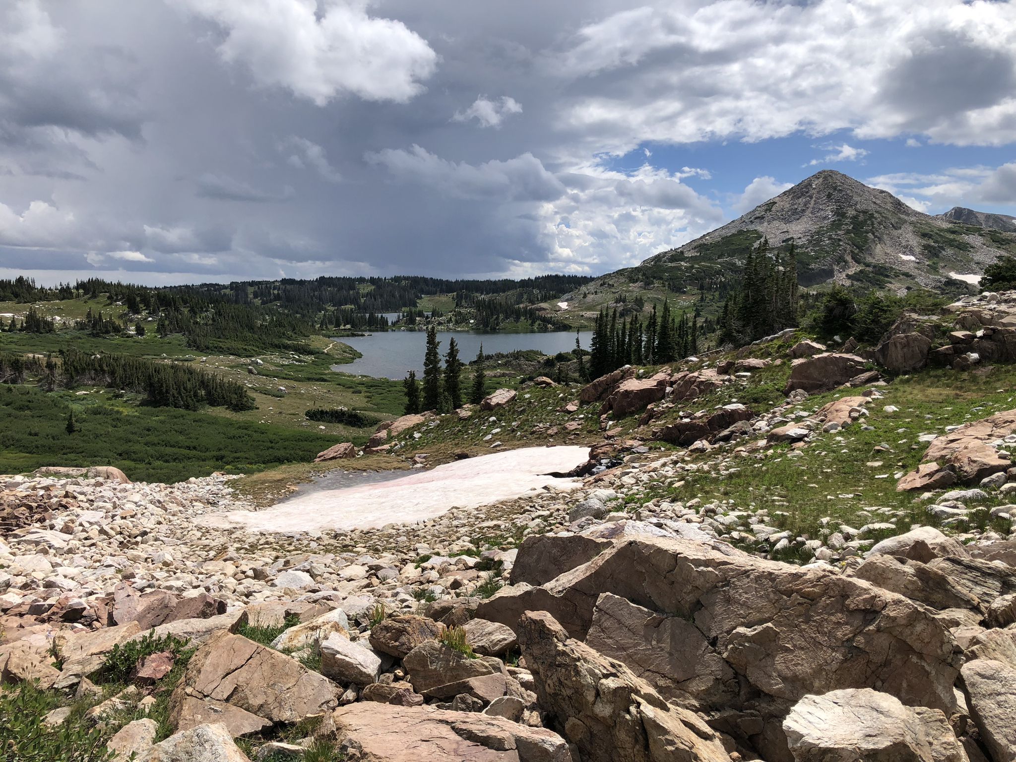 Mountain lake, green hills, rocky foreground, and cloudy sky. - Gap Lakes Trail