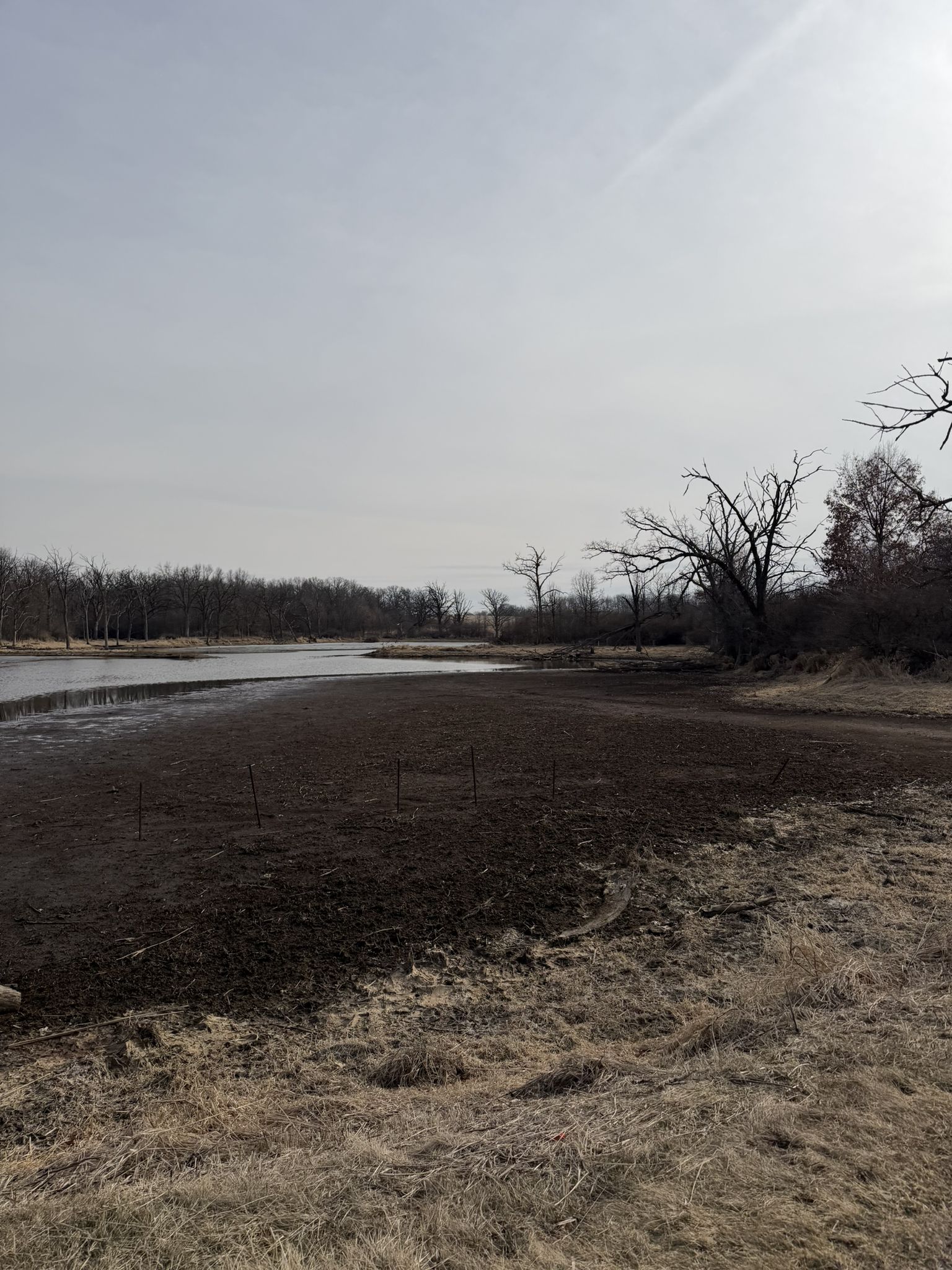 Exposed muddy ground next to a calm water body under an overcast sky. - Military Ridge State Trail – Dawley Conservancy Park loop from Capital Springs State Recreation Area- Jenni & Kyle Unit