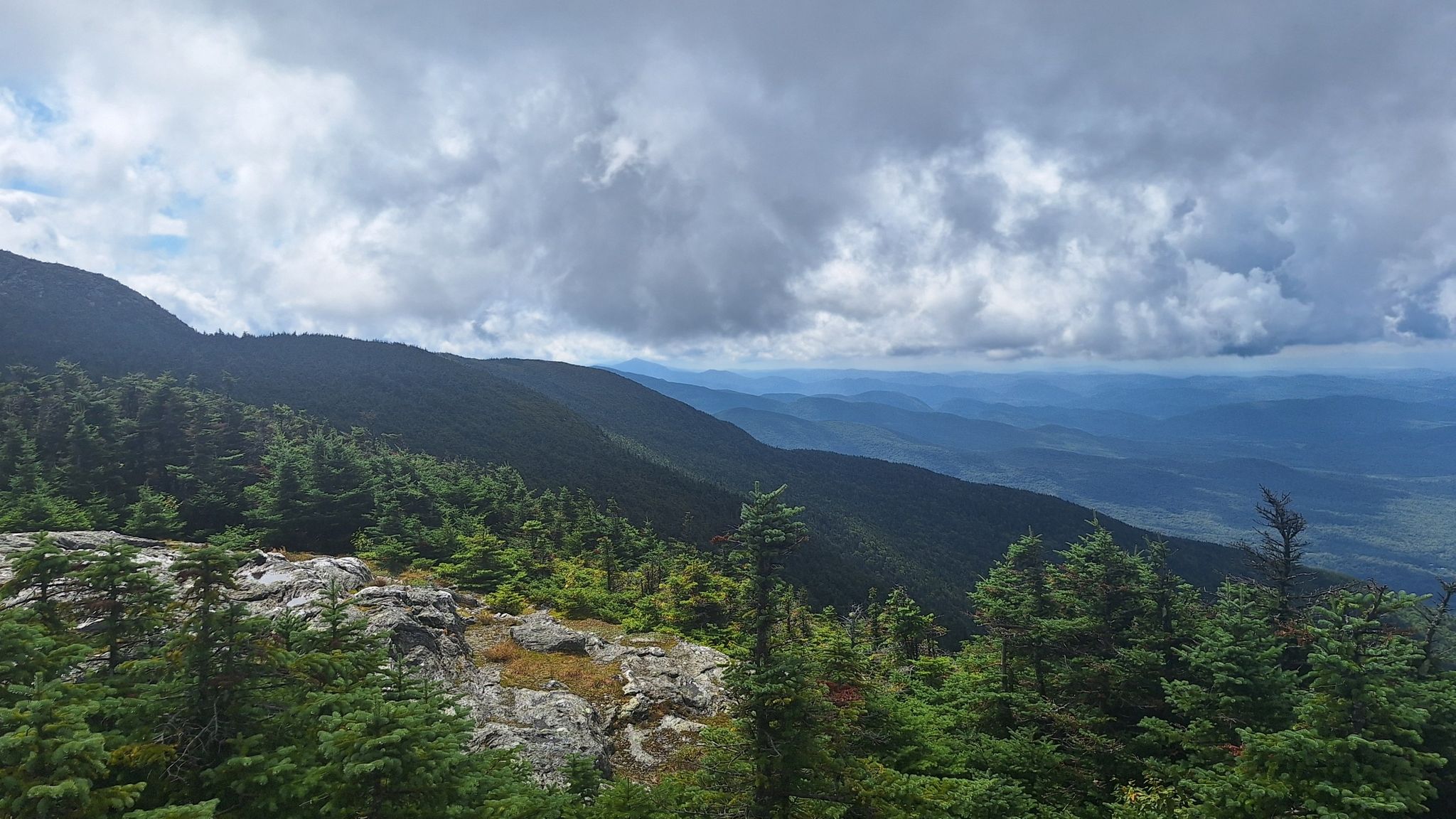 Cloudy mountain view with green forests, rocky terrain, and distant peaks. - Maple Ridge and Sunset Ridge Loop