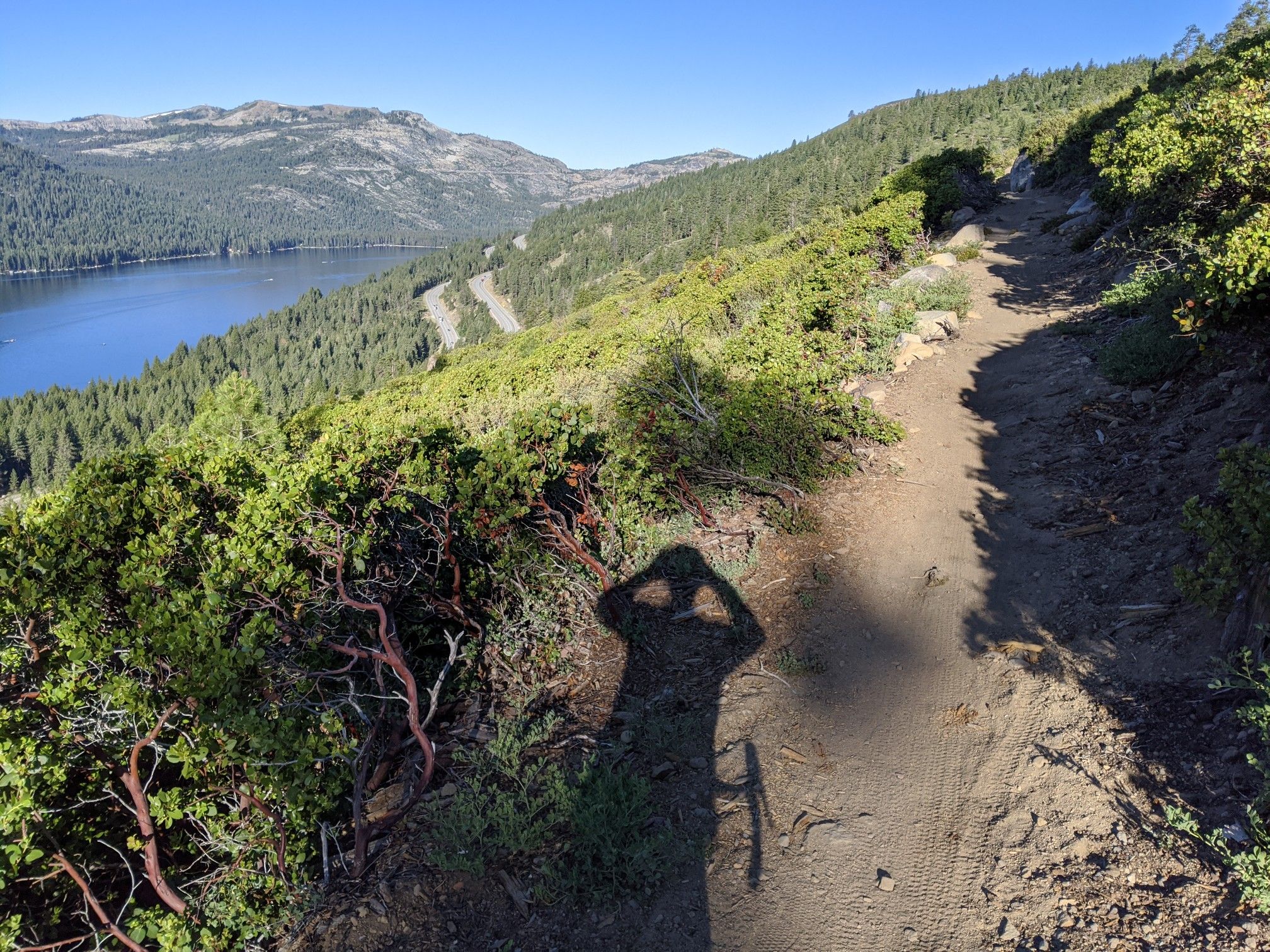 Shadow of a person on a dirt trail overlooking a lake and forested hills. - Running loop from Bermgarten Parking