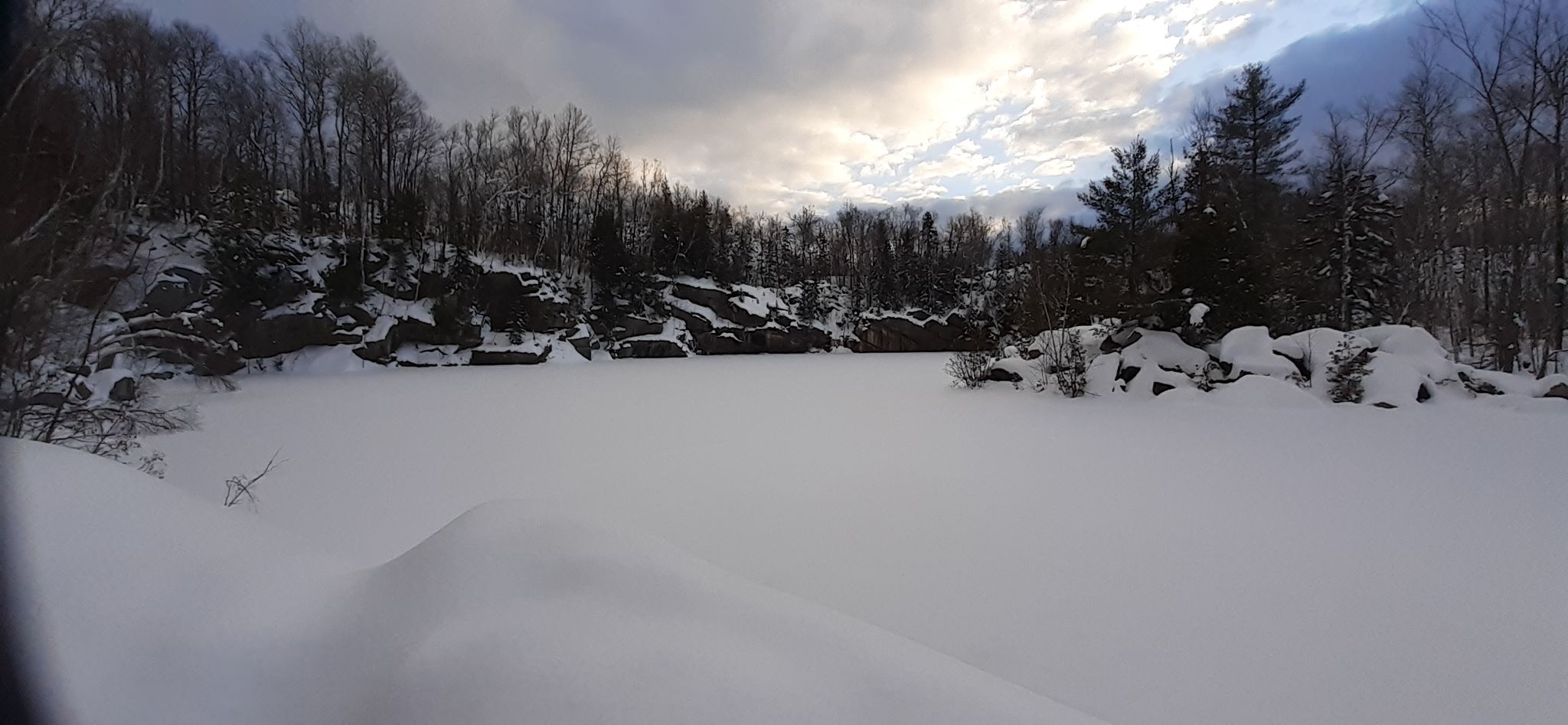 Panoramic view of a vast snow-covered frozen lake surrounded by winter trees. - Westside and Serenity Trail Loop