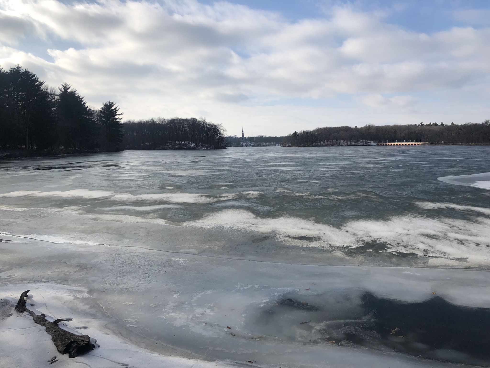 Partially frozen lake under a cloudy sky, with distant trees and shore. - Saint Mary's Lake loop via Lakeshore Drive