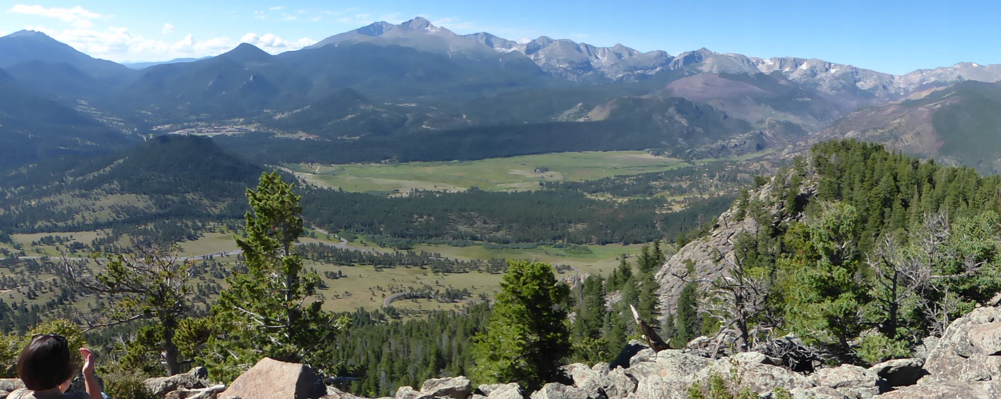 Panoramic view of a vast mountain range, green valley, and forests under clear skies. A person observes. - Deer Mountain Loop Trail